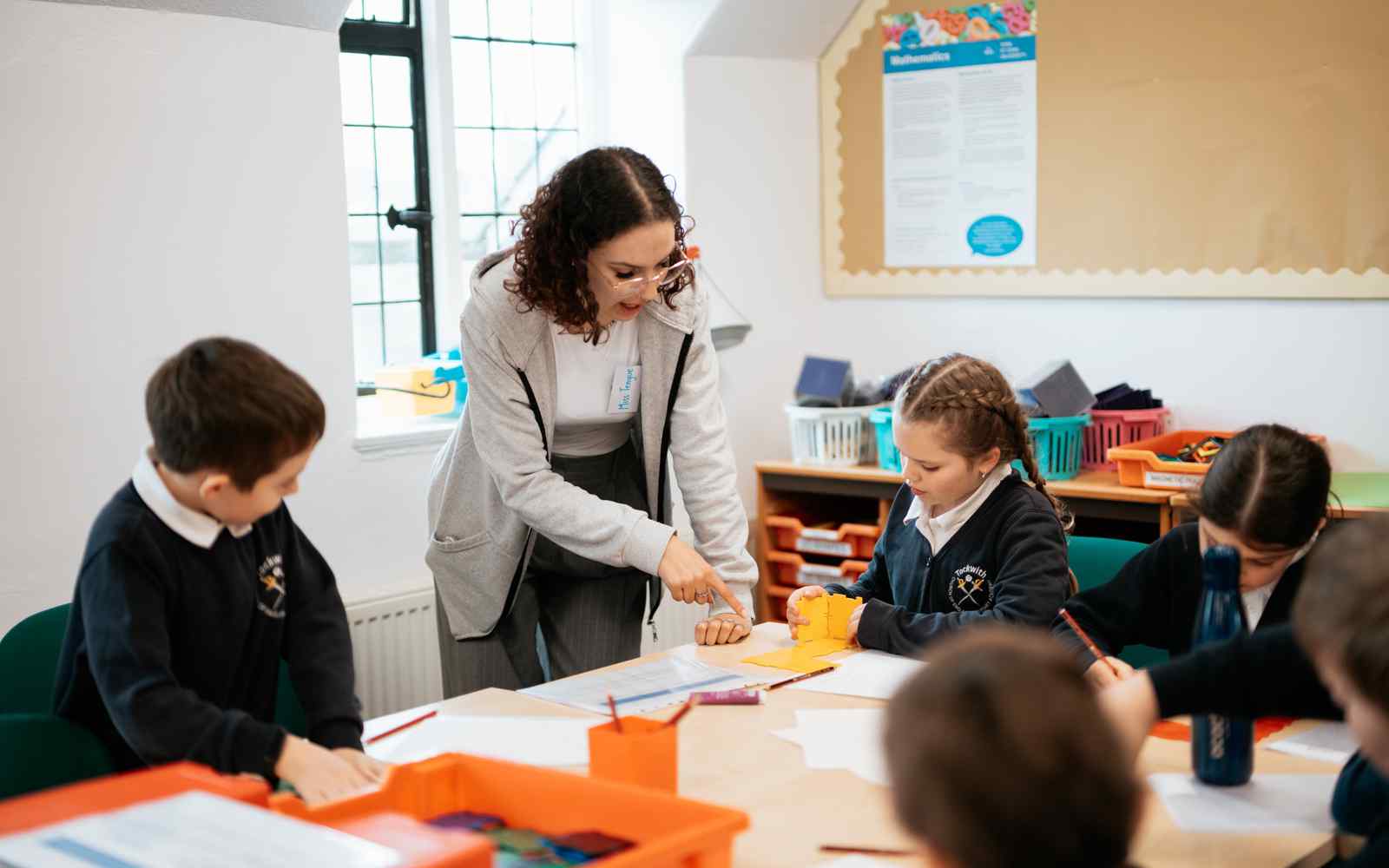 Female trainee teacher attending a table of children in class