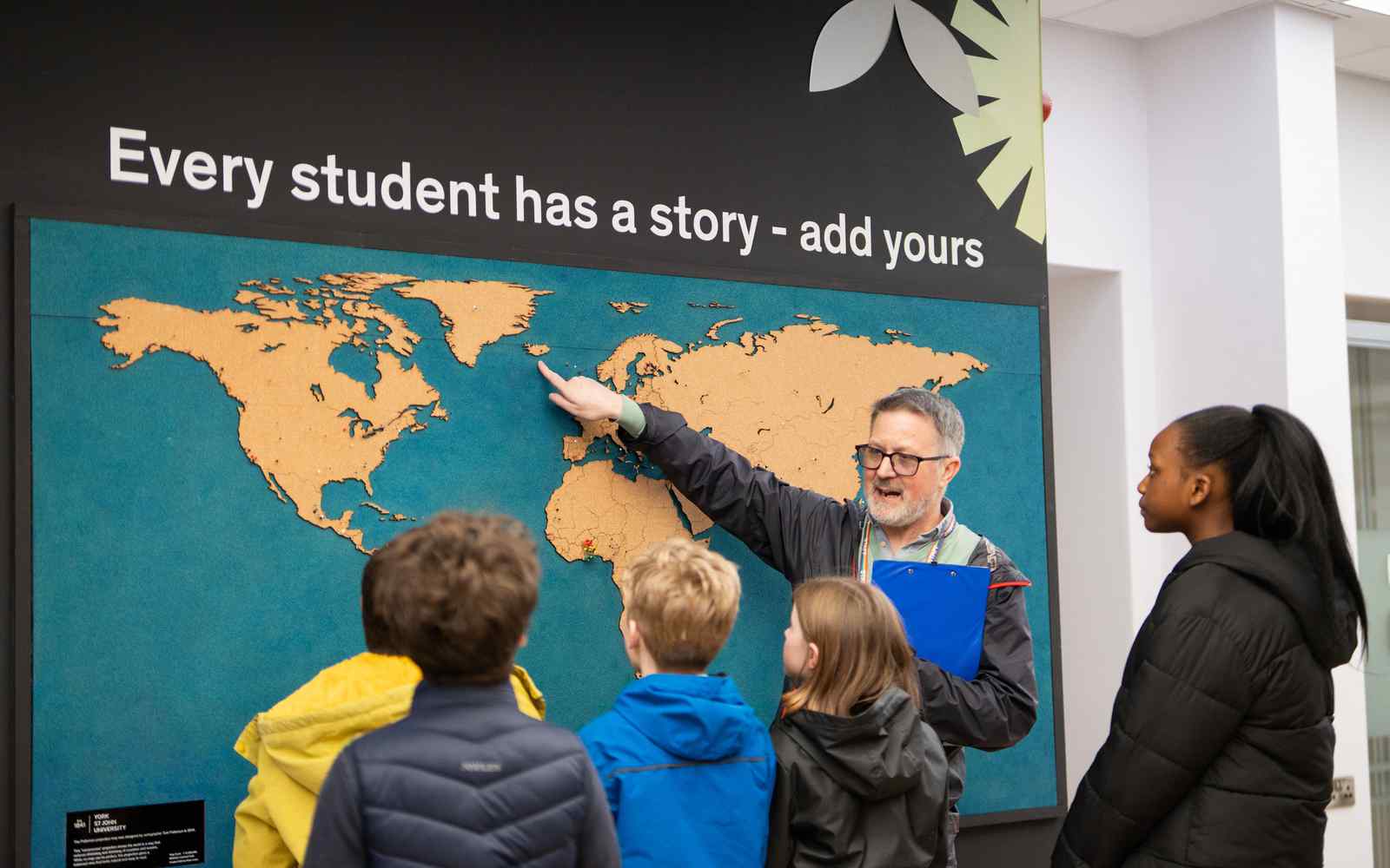 Male teacher showing an image of an atlas on the wall to a group of children