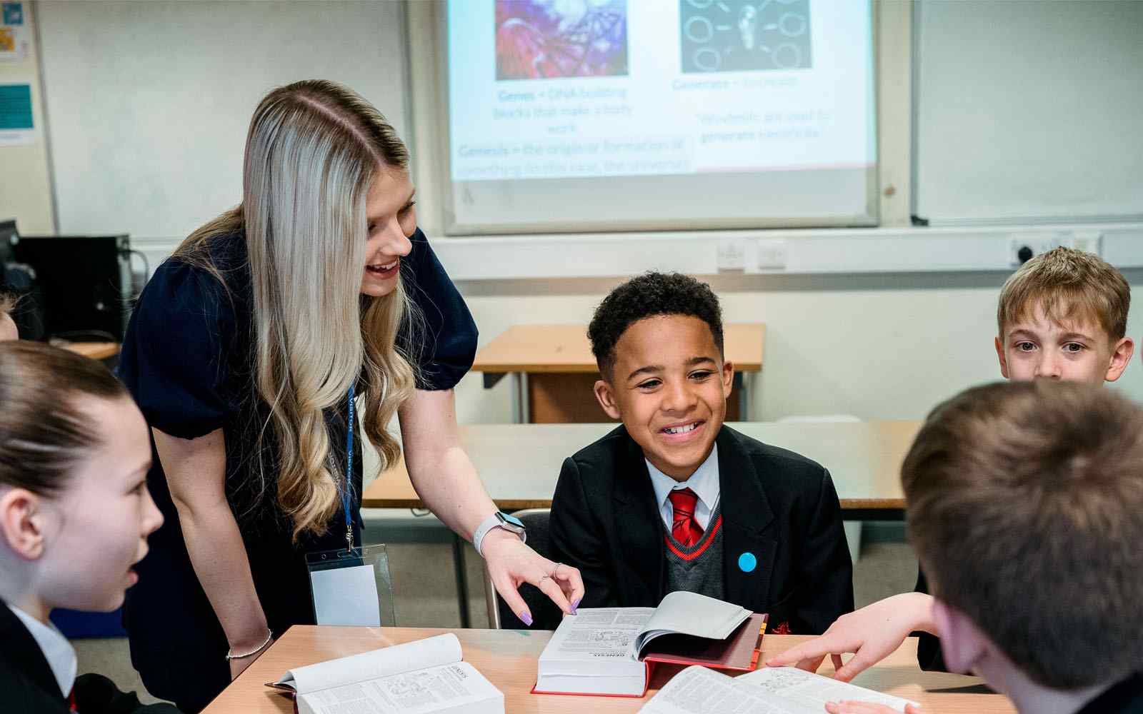 young male student in school uniform smiling at classroom desk