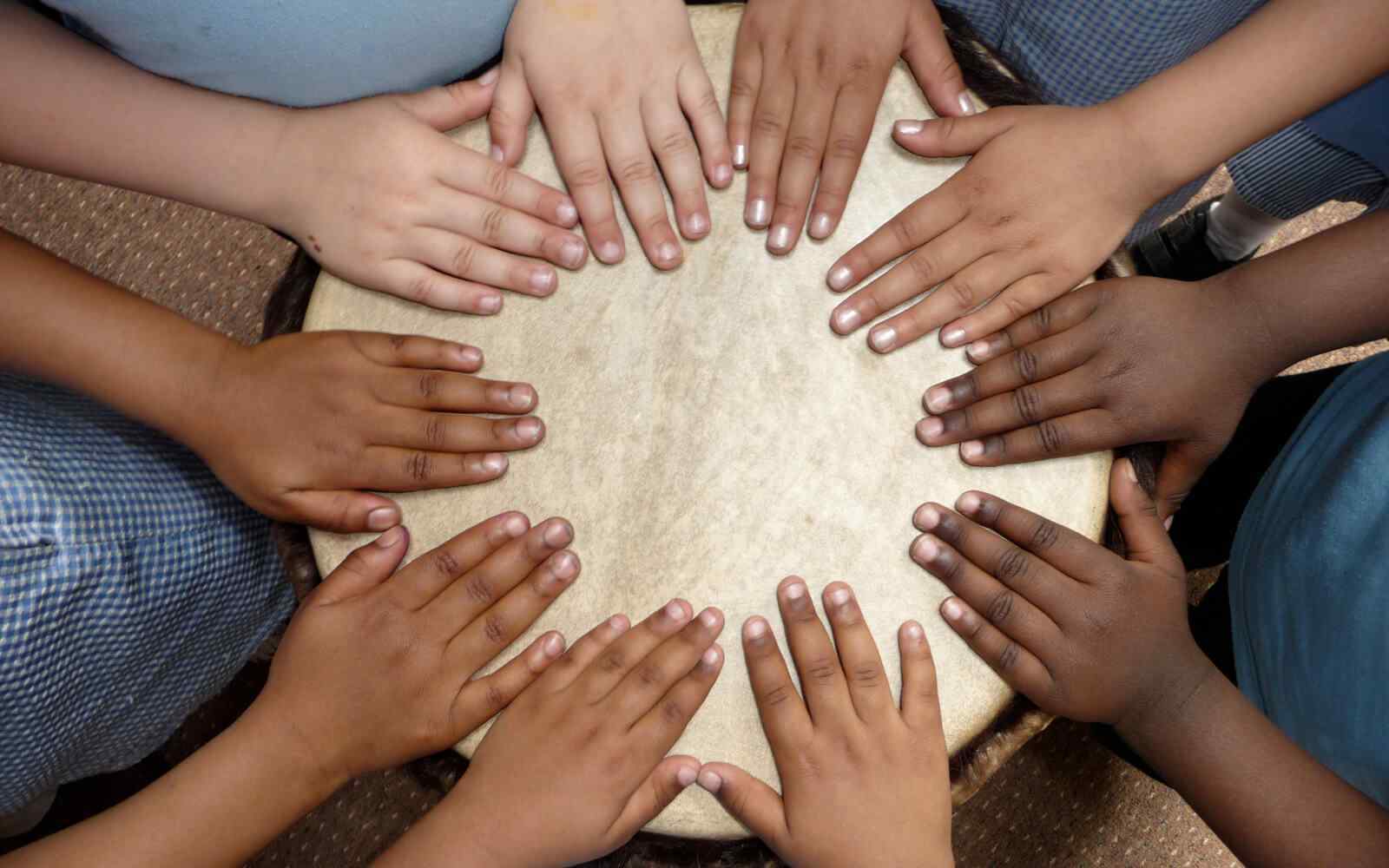 A circle of hands placed on the top of a drum.