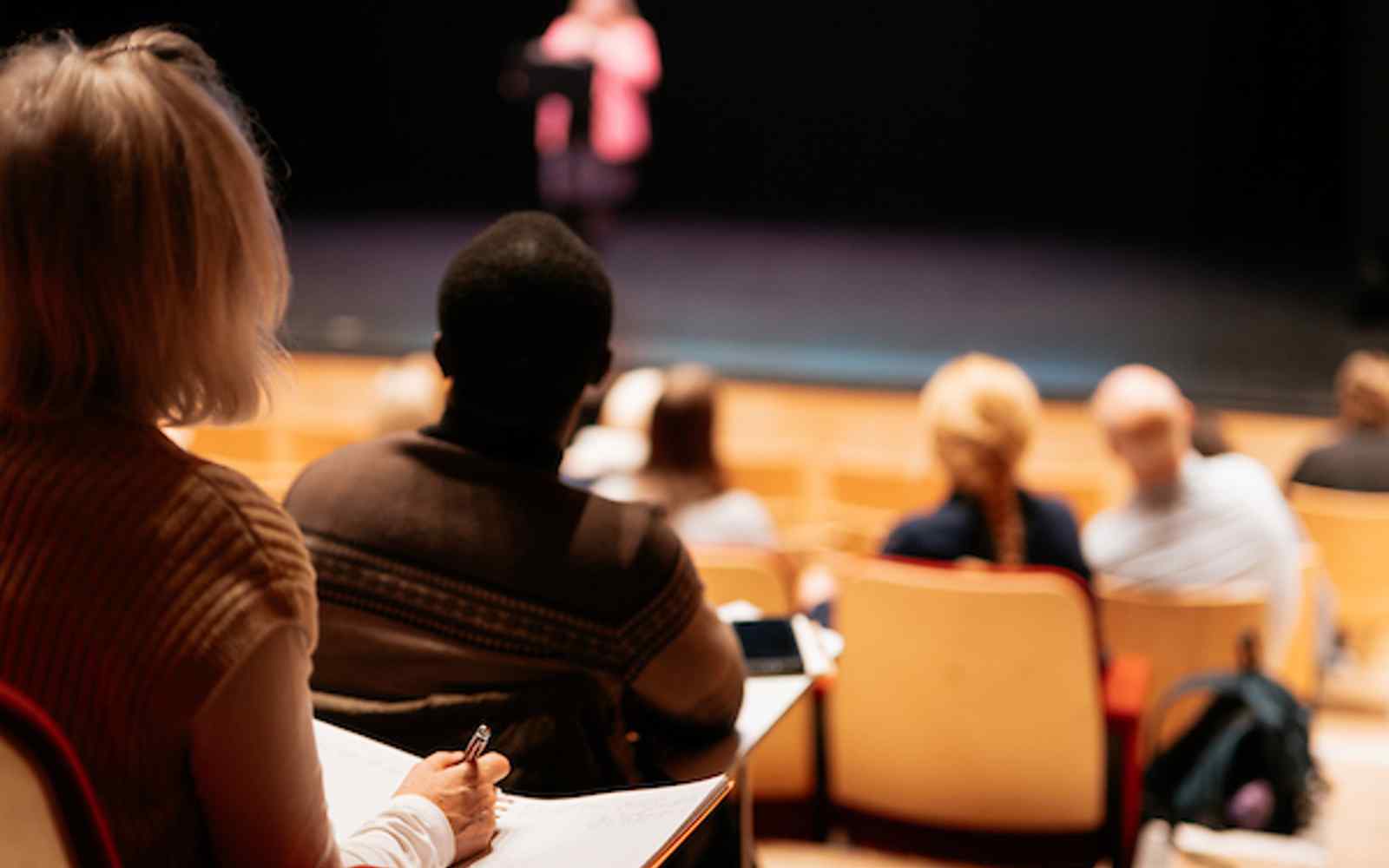An audience sat in an auditorium, with a presenter speaking on stage.