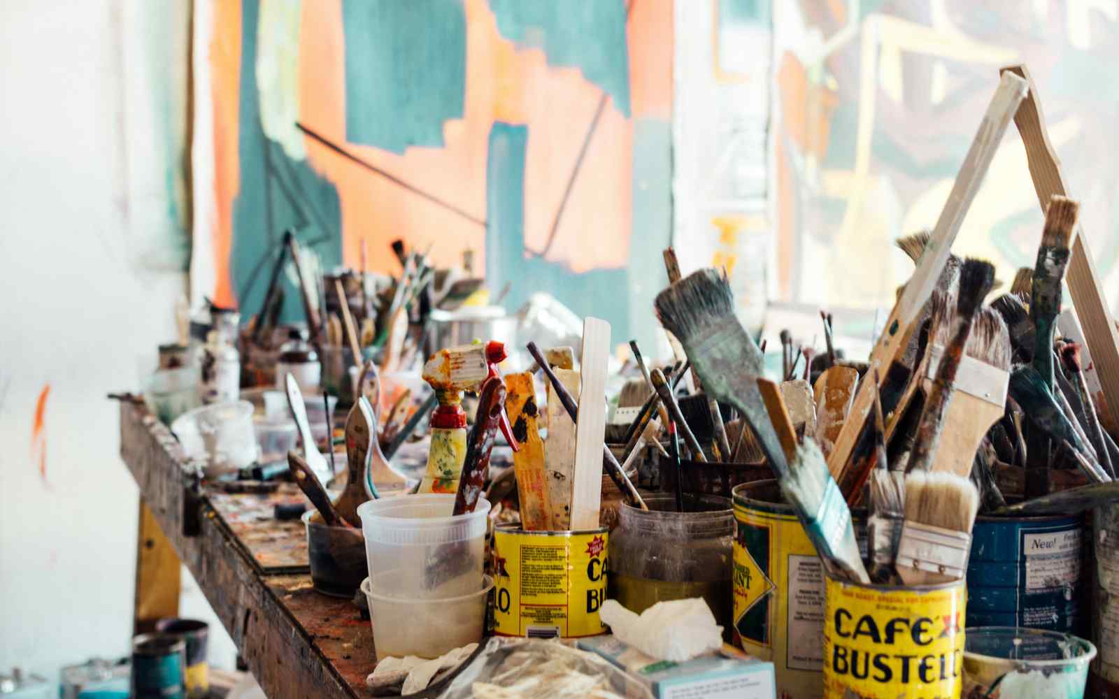 Paint cans and dirty brushes on a long wooden table.