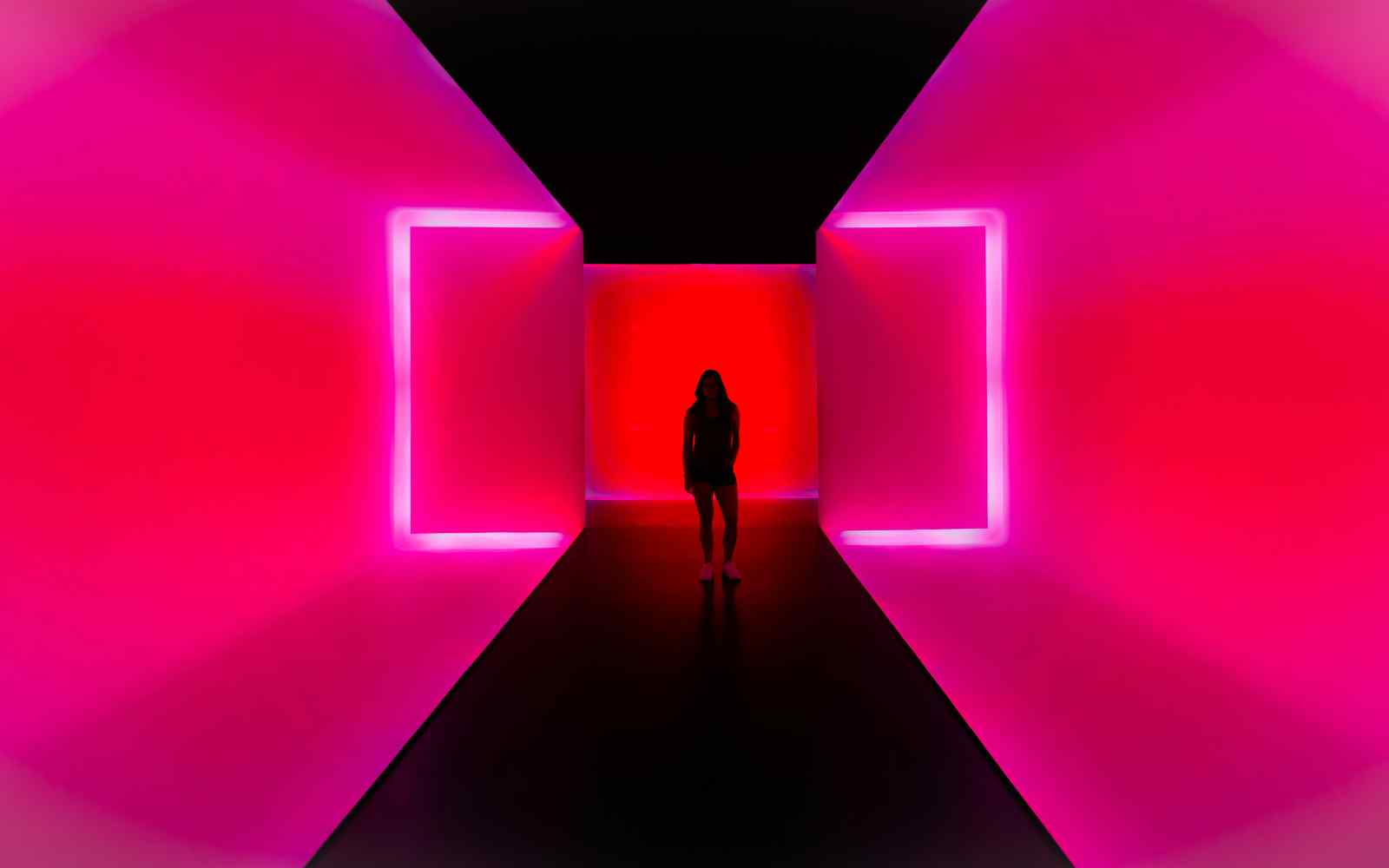 Pink neon room with an individual stood at the end of a hallway.