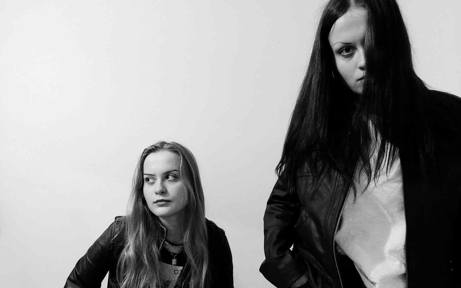 Black and white image of two women, one seated and one standing in the foreground looking at the camera