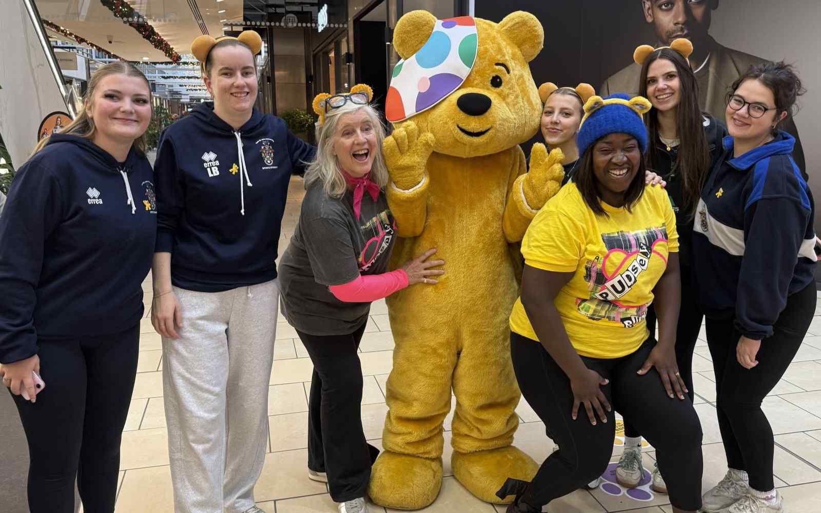 A group of people in sportswear gathered round a giant cuddly bear
