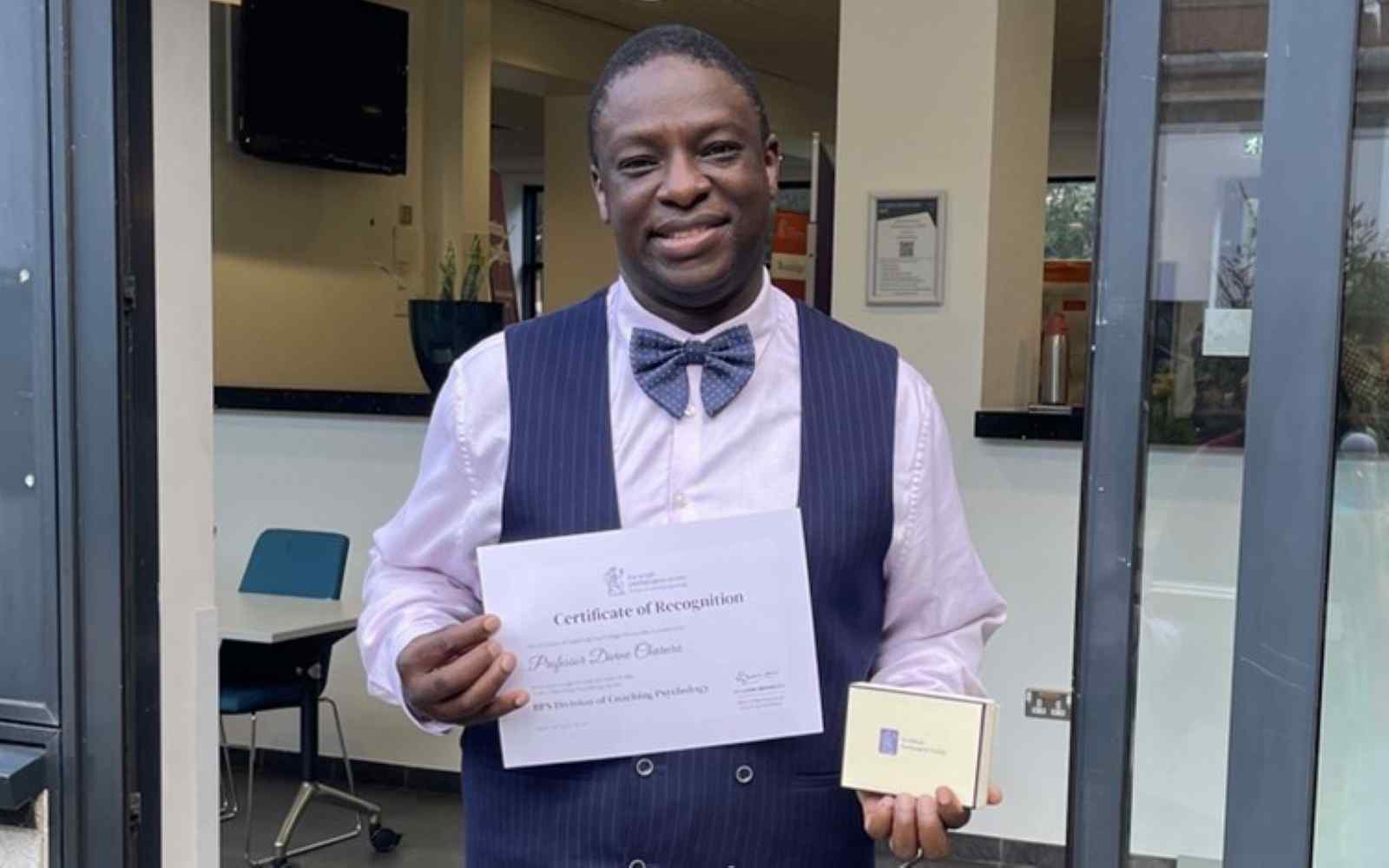 A male looking straight forward holding a plaque and certificate