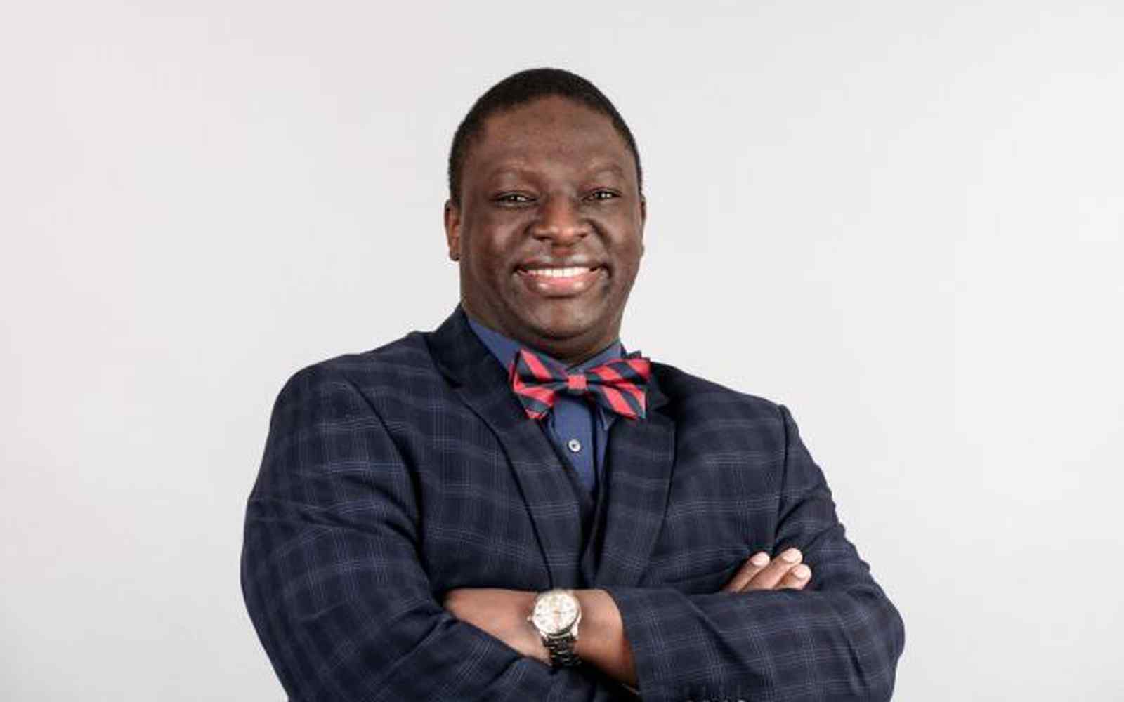 Man in bow tie smiling at camera, with white backdrop