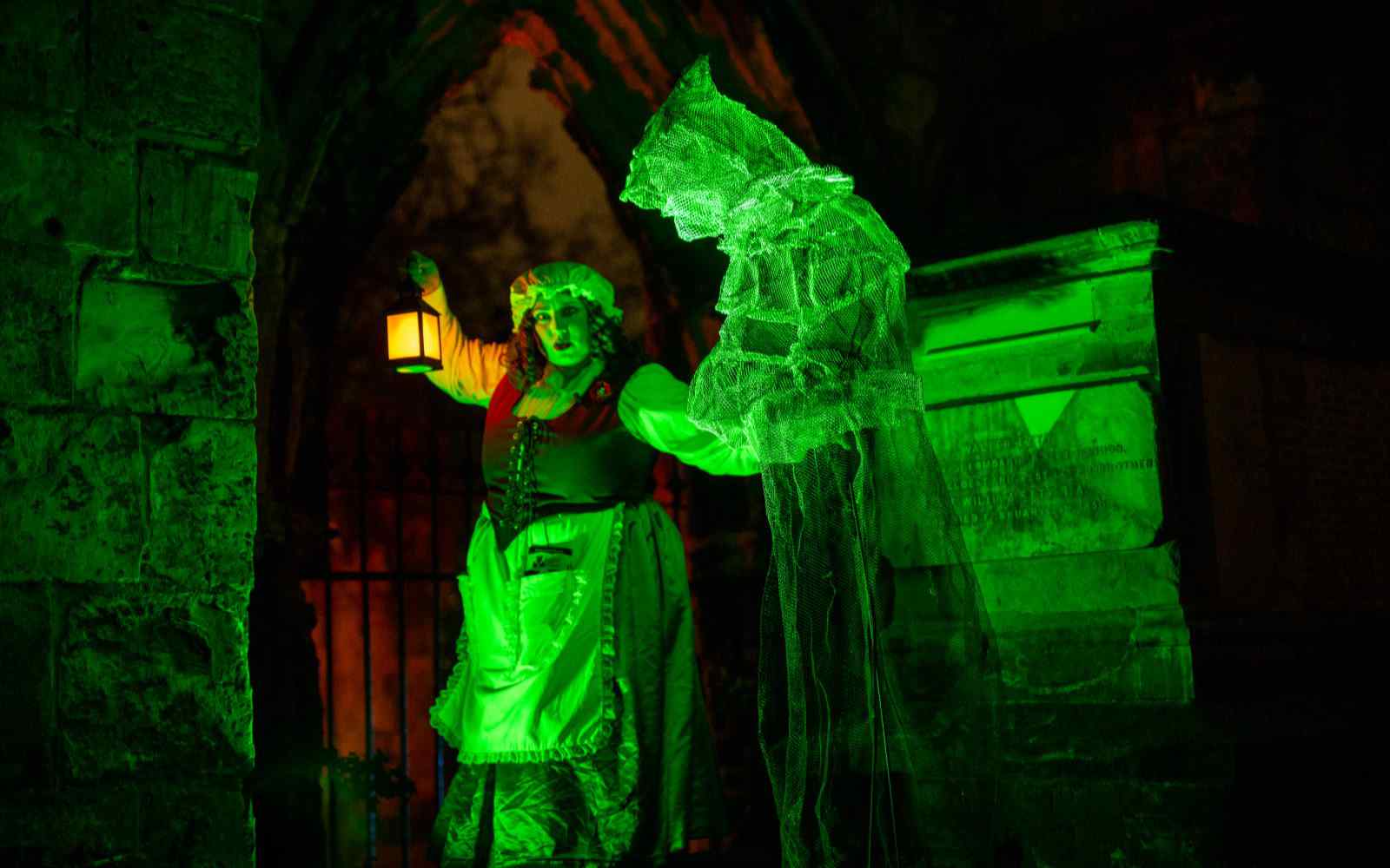 A person dressed up as a maid next to a wire mesh figure in the dark and lit up with green lights