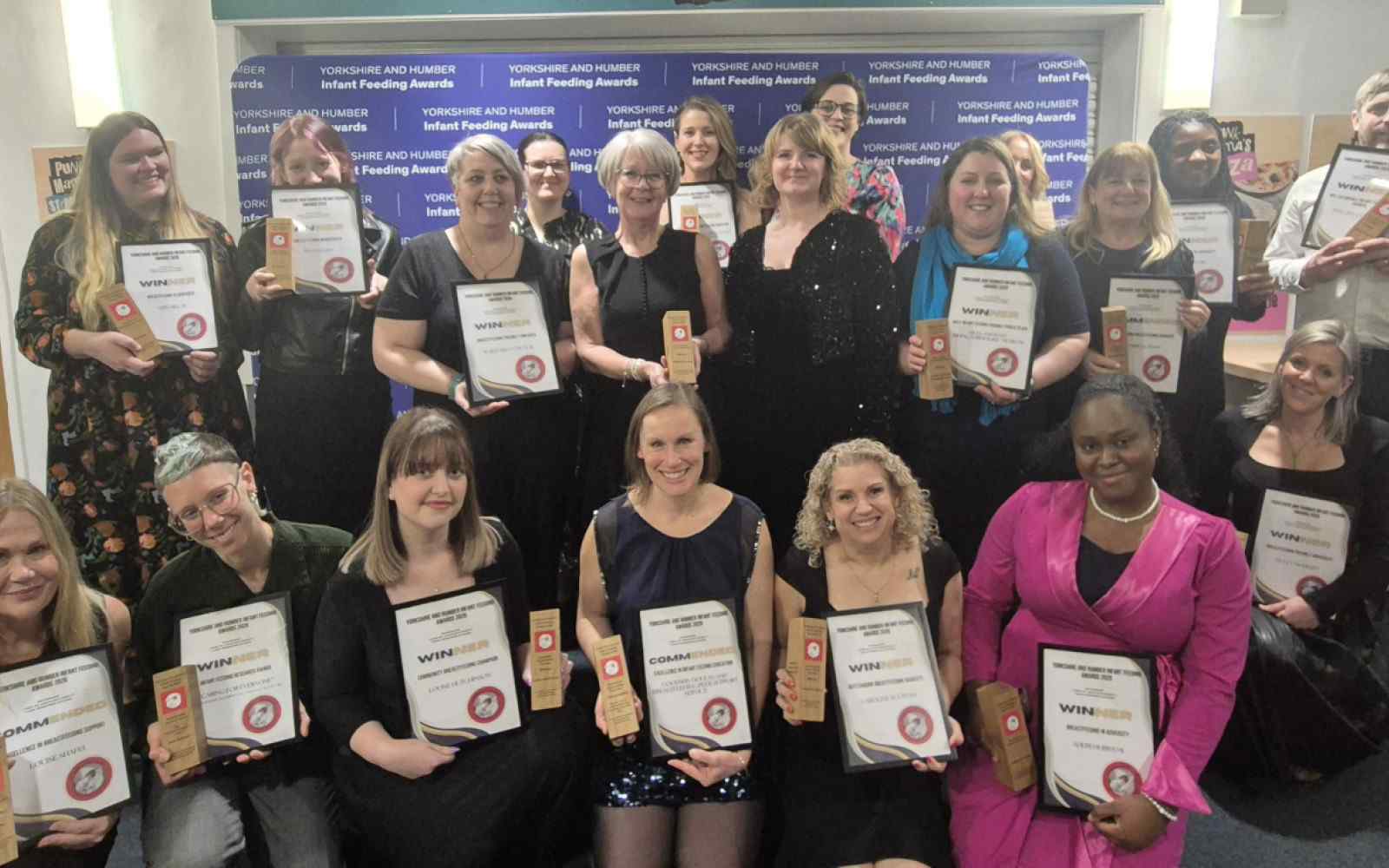 A group of 20 people holding award certificates against a backdrop that says Yorkshire and Humber infant feeding awards