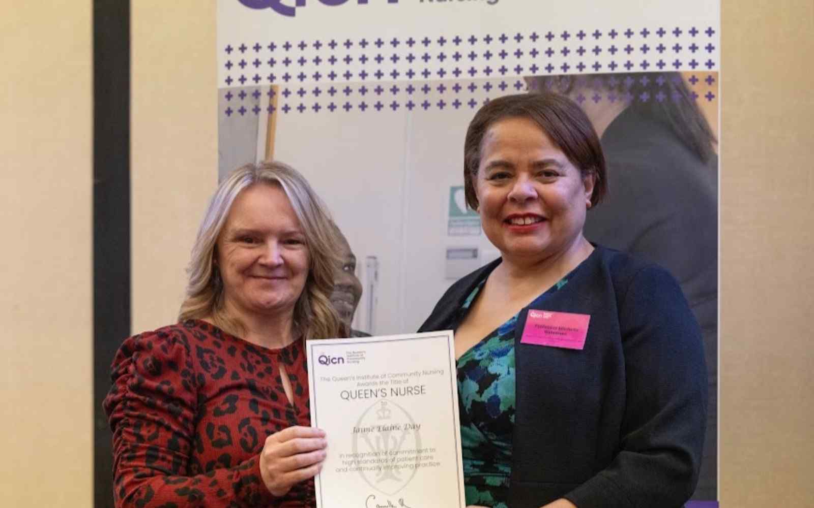 2 women standing in front of a pull up banner holding a certificate