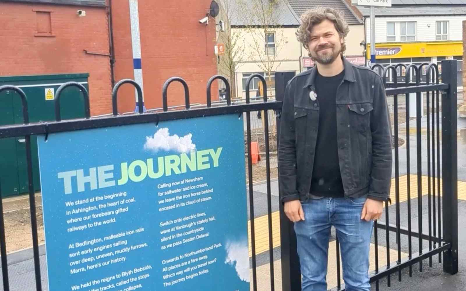 John Challis standing beside a display of his poem on the railings of a railway platform
