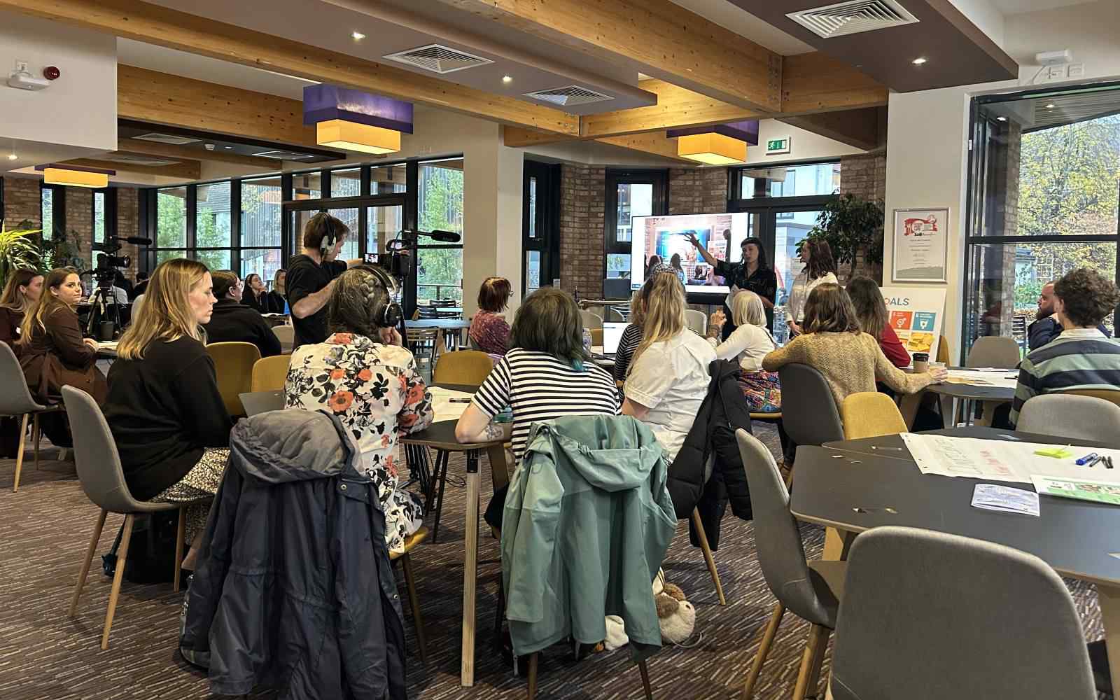 Students present sustainability work to a crowd sitting at tables