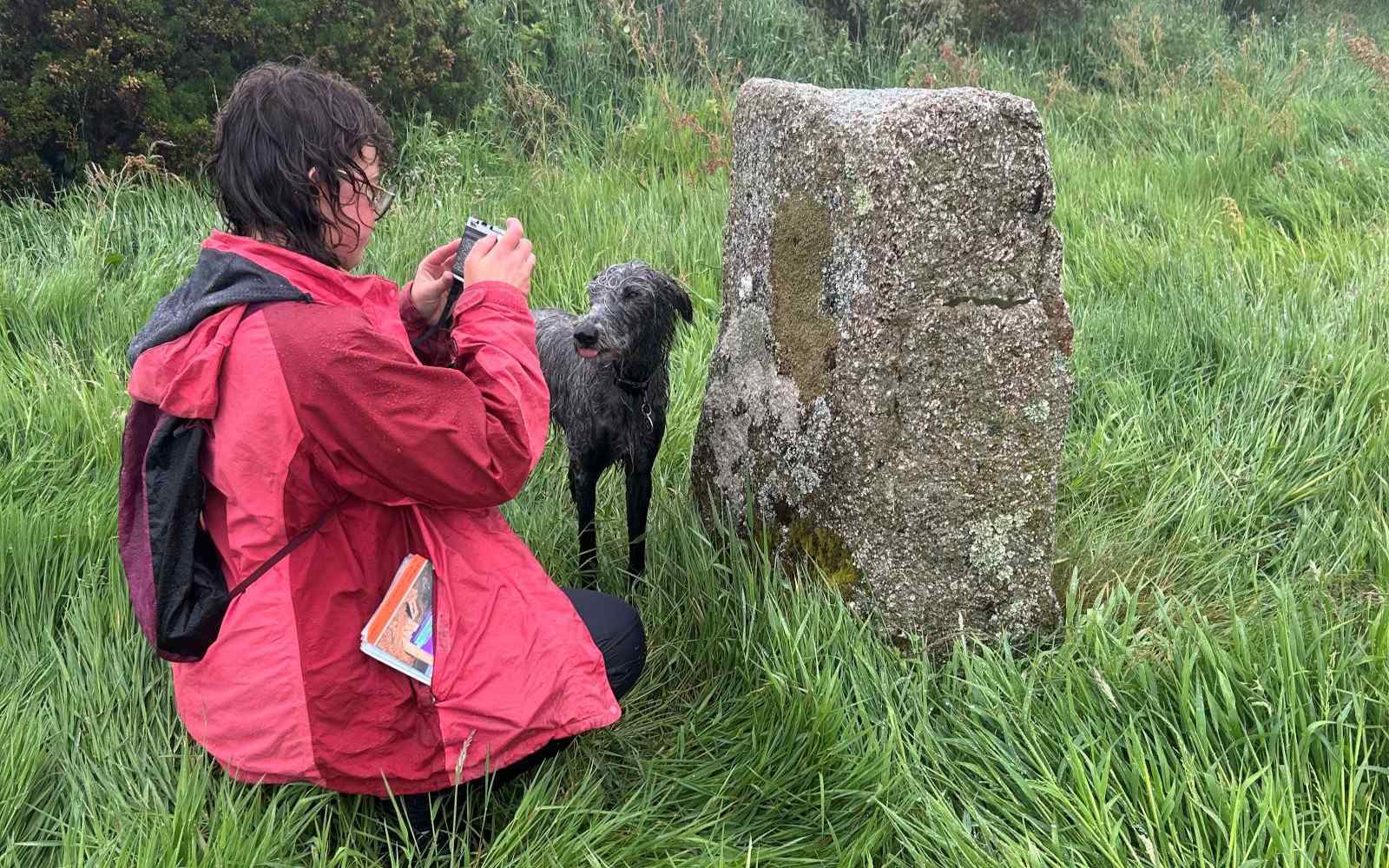 A student with her dog taking a photograph of a stone at a stone circle