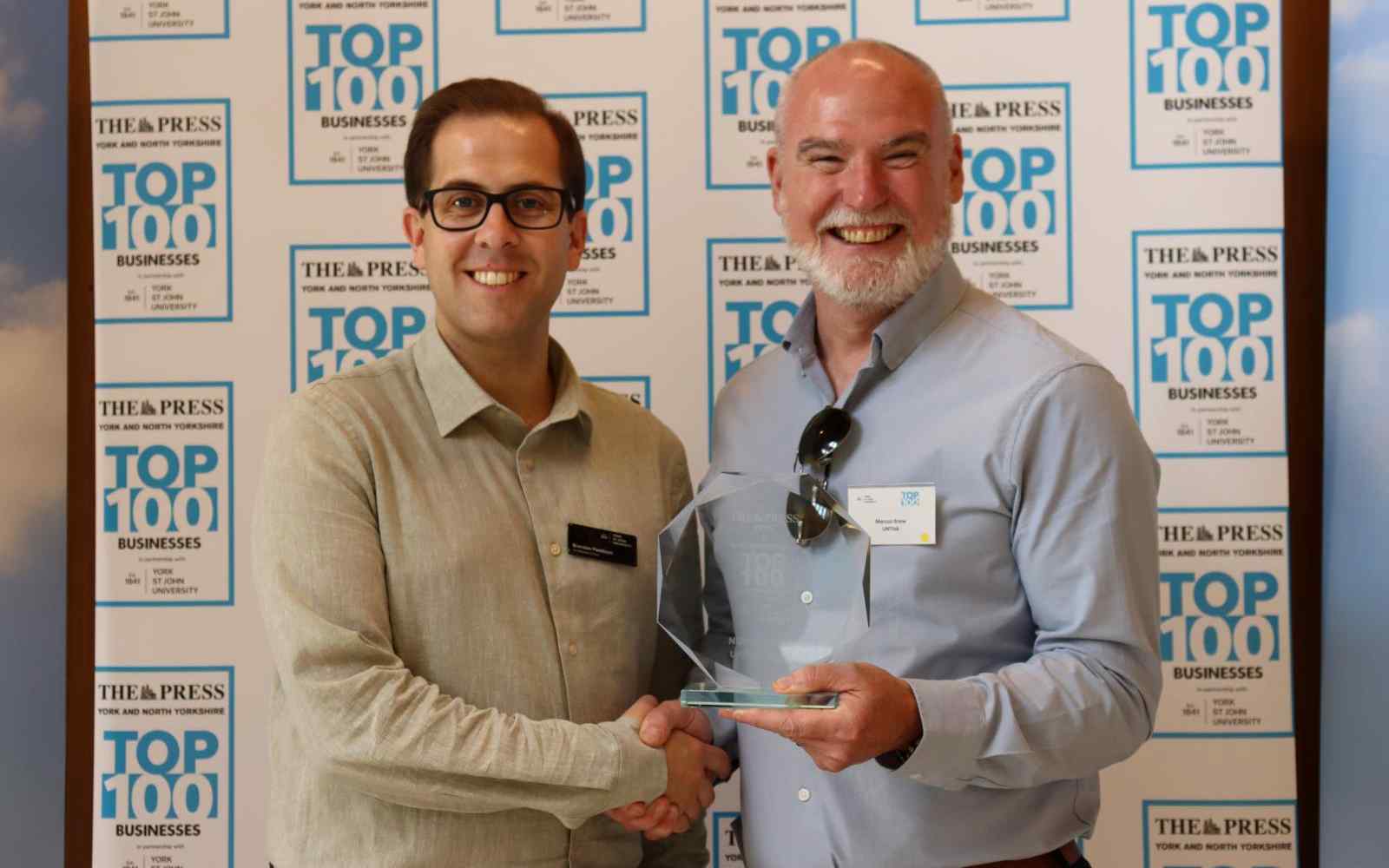 2 men jointly holding a glass award in front of a Top 100 branded backdrop