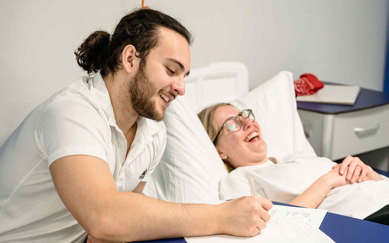 A student takes notes next to a patient in a hospital bed