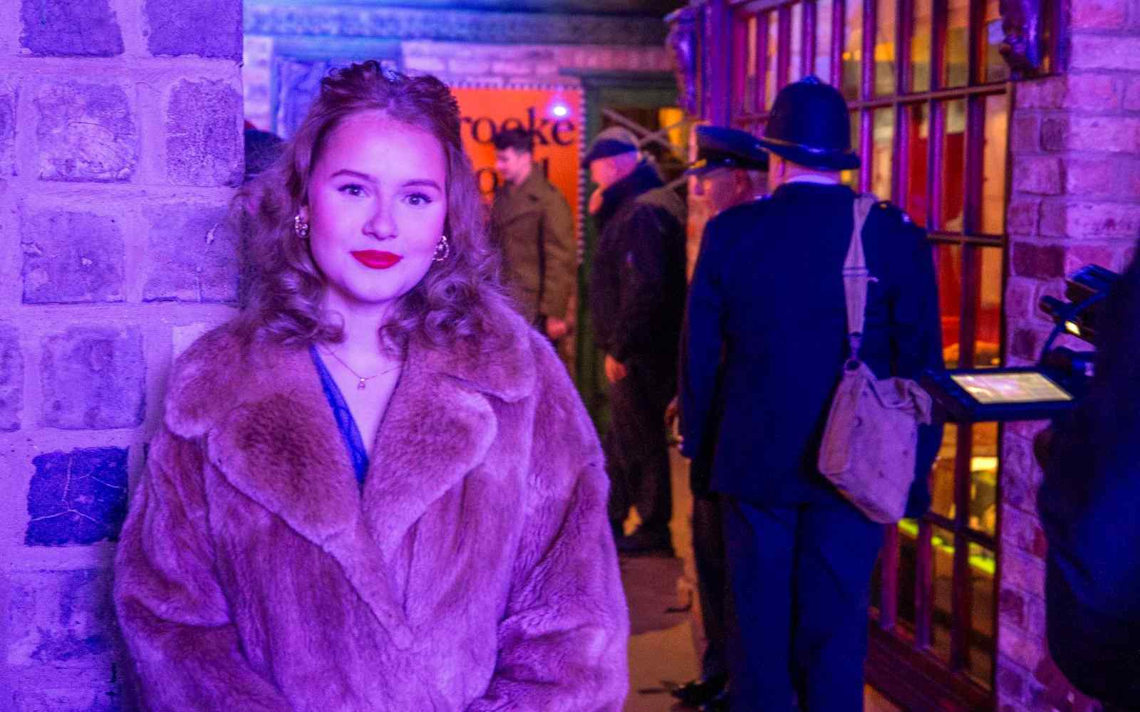A student in 1940s clothing in a recreated vintage shop front scene