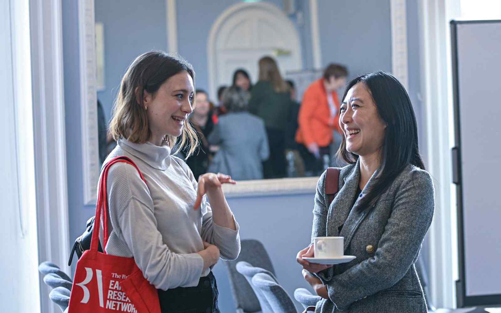 2 women talking at an event, one has a red tote bag with the words early career research network