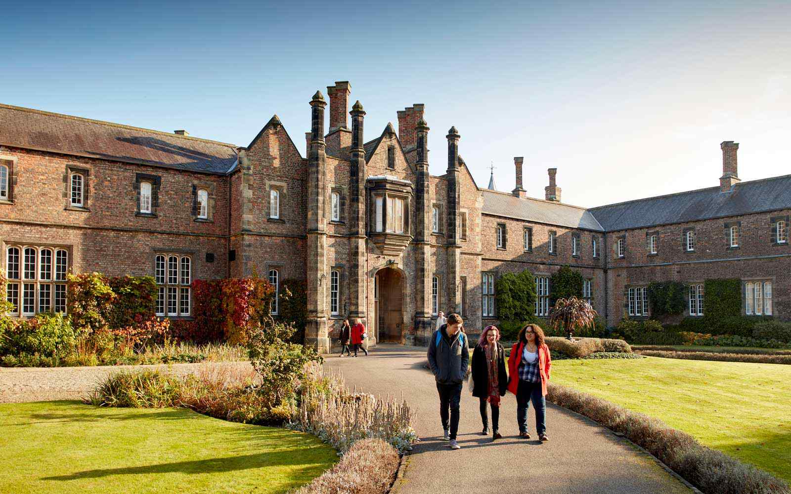 Three students walk together outside the historic Lord Mayor's Walk campus building, in the sun.