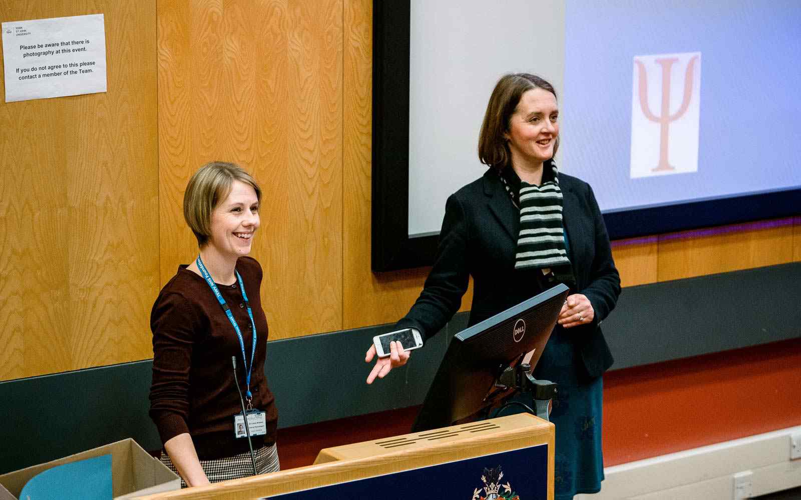 Two lecturers at the front of a lecture theatre smiling 