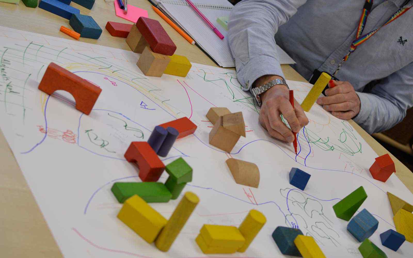 A staff member drawing on a piece of paper that has wooden blocks on top of it.