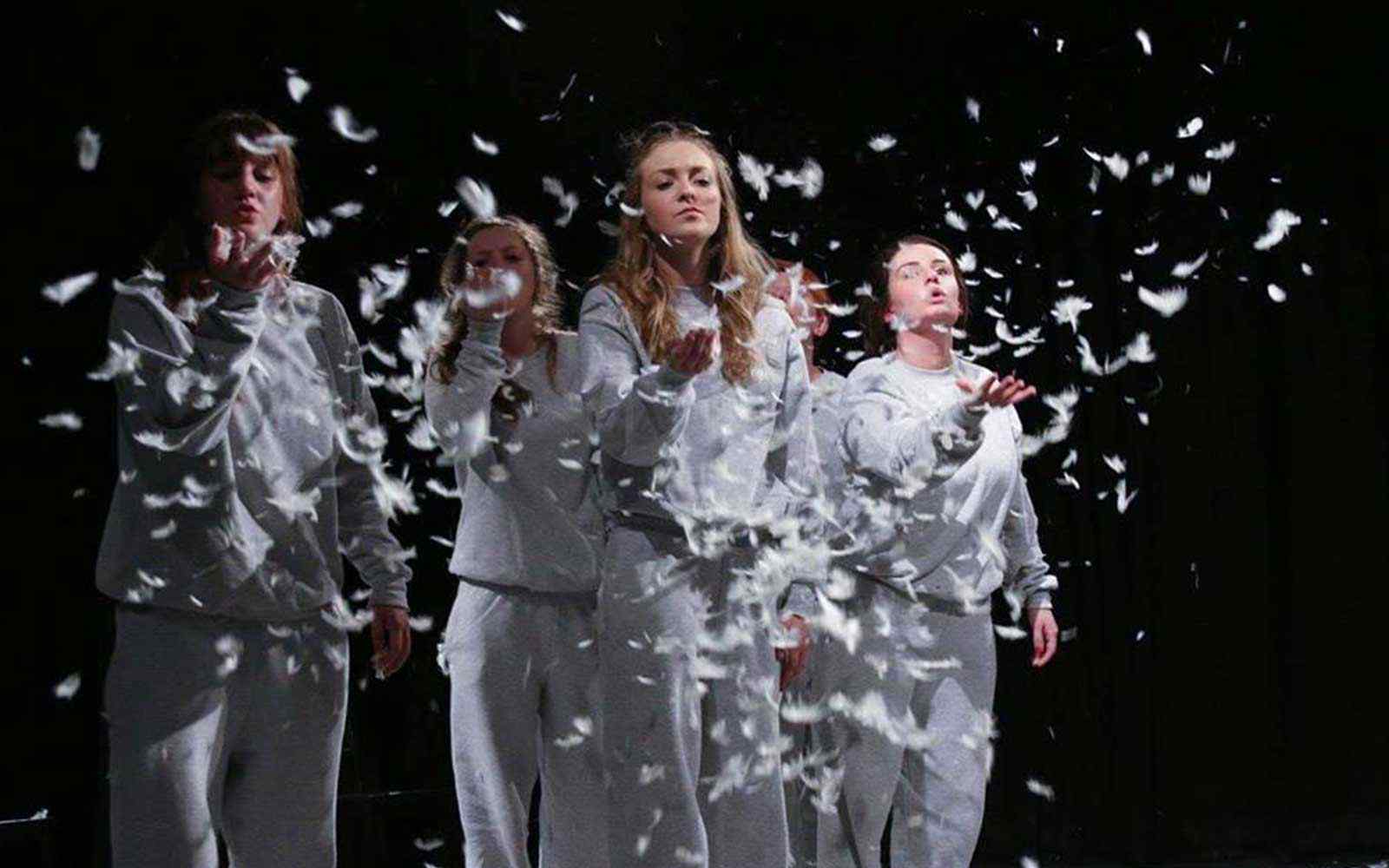Drama students surrounded in white feathers during a performance.