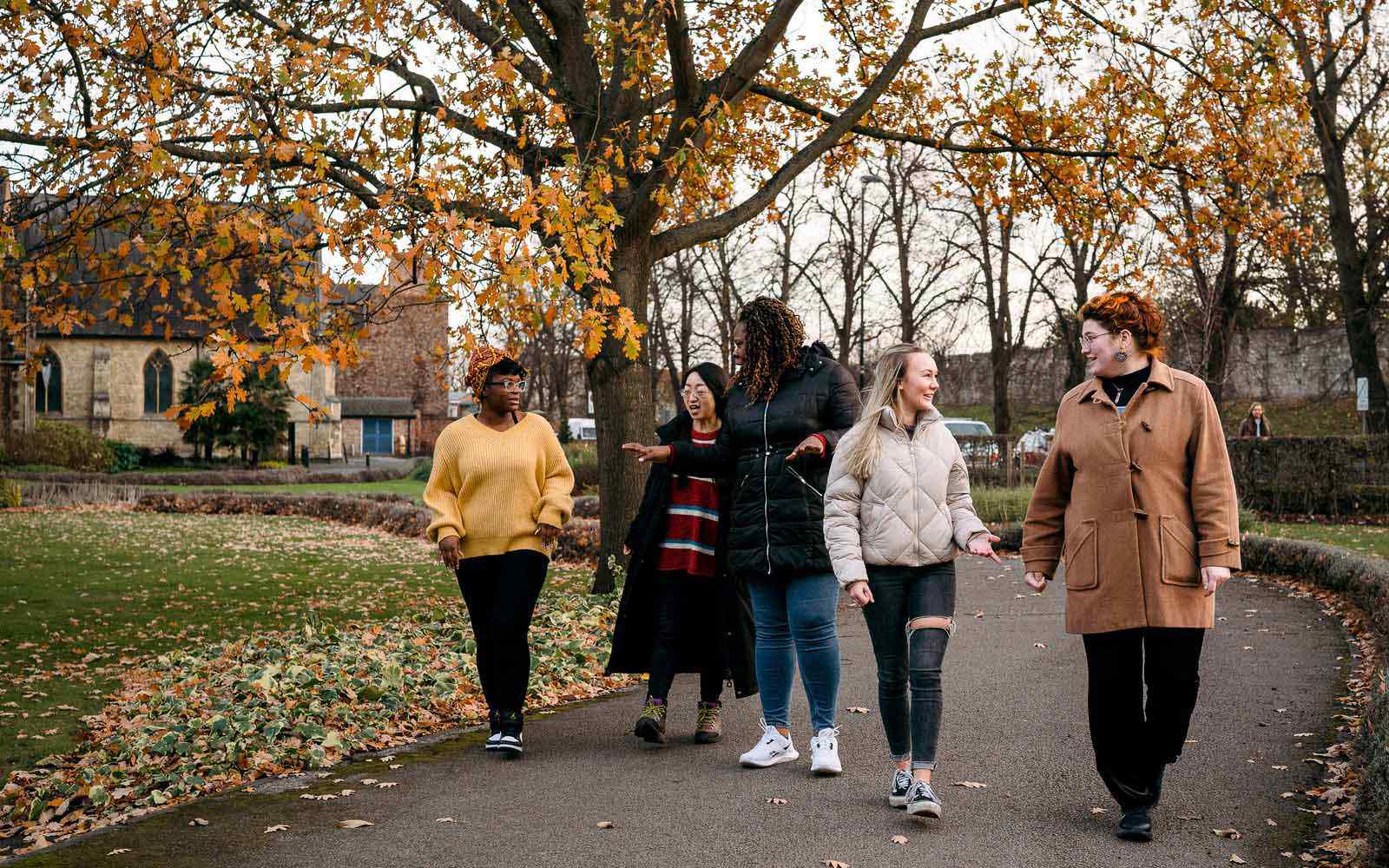 Five students walk together through autumnal trees on campus.