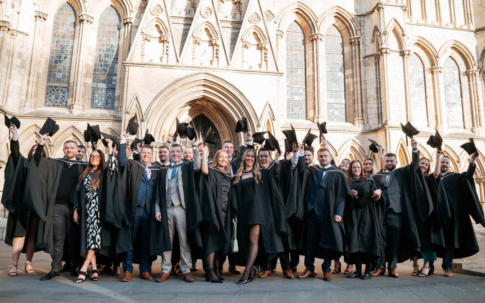 Large group of new graduates raising their caps outside York Minster.