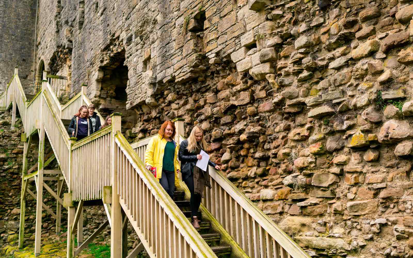 Two students walking down wooden steps in an abbey 