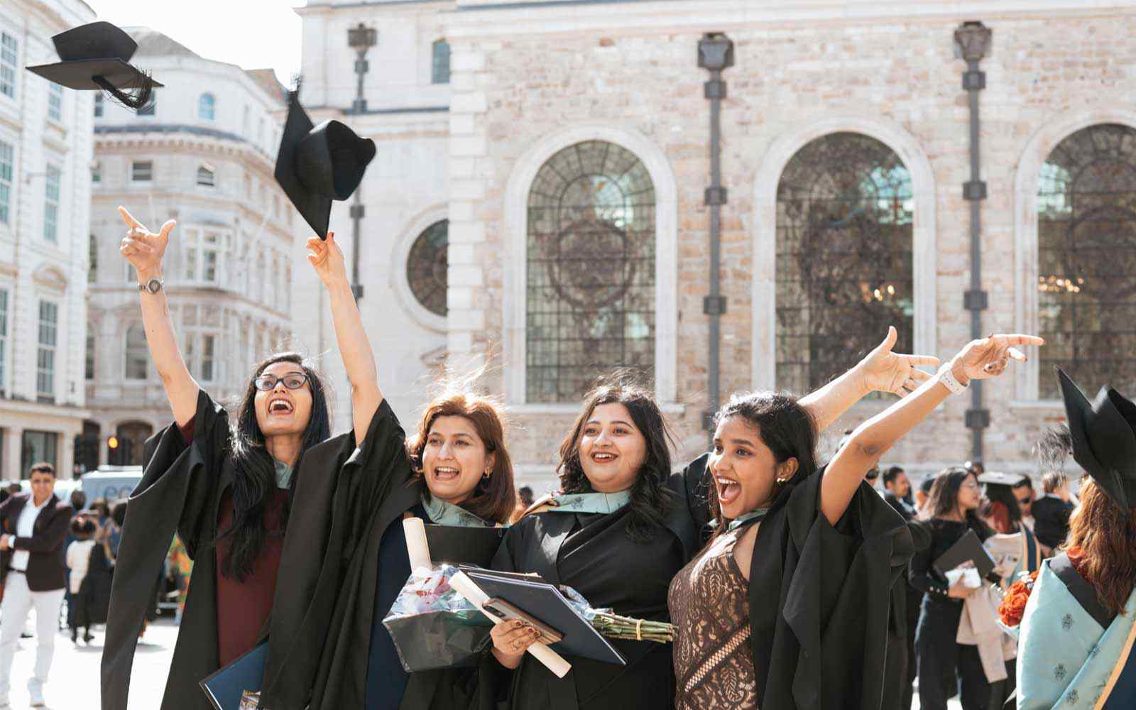 Four students throw their caps in the air at a London Campus graduation ceremony.
