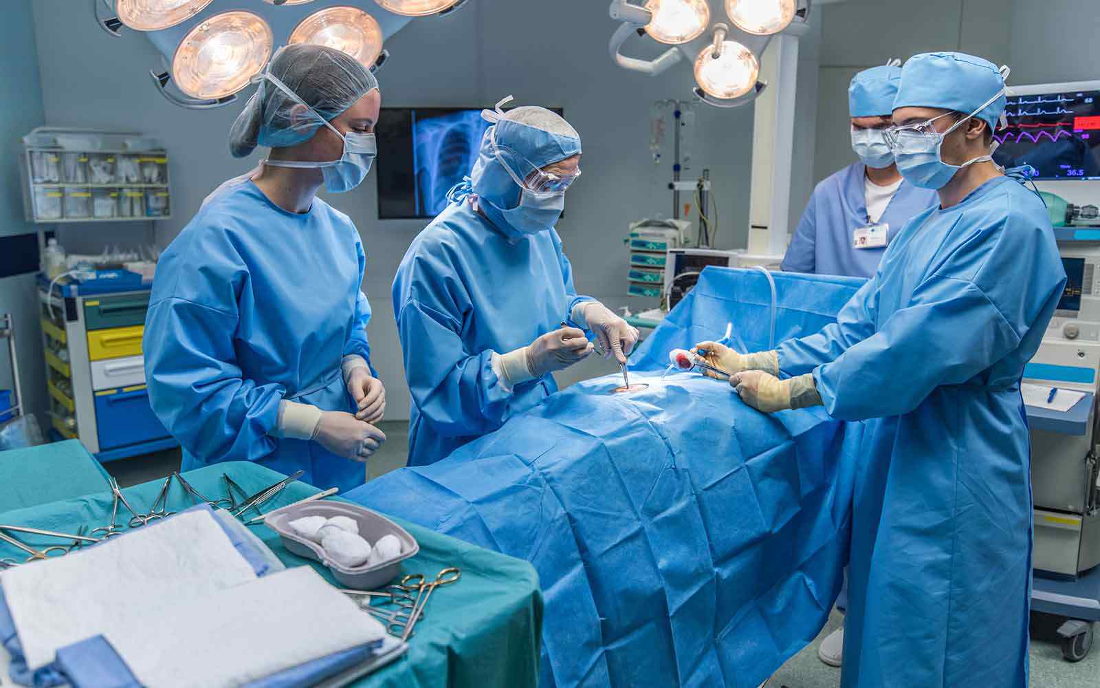 Students wearing medical scrubs perform surgery on a dummy in a mock operating theatre