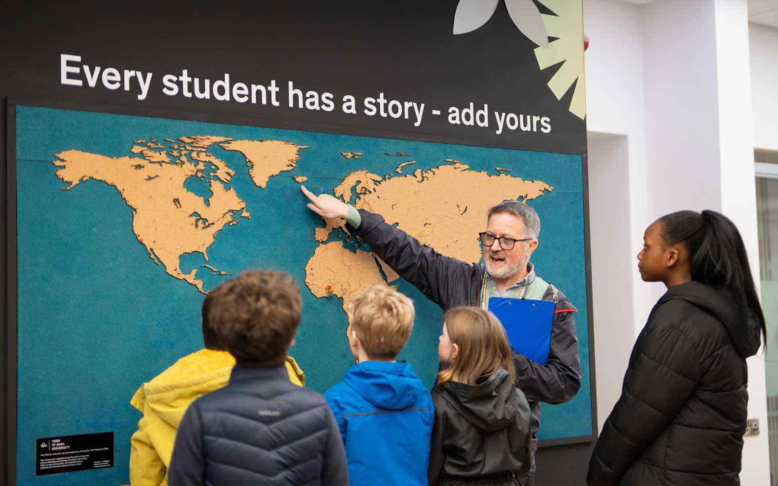 Male teacher showing a wall map to a group of children.