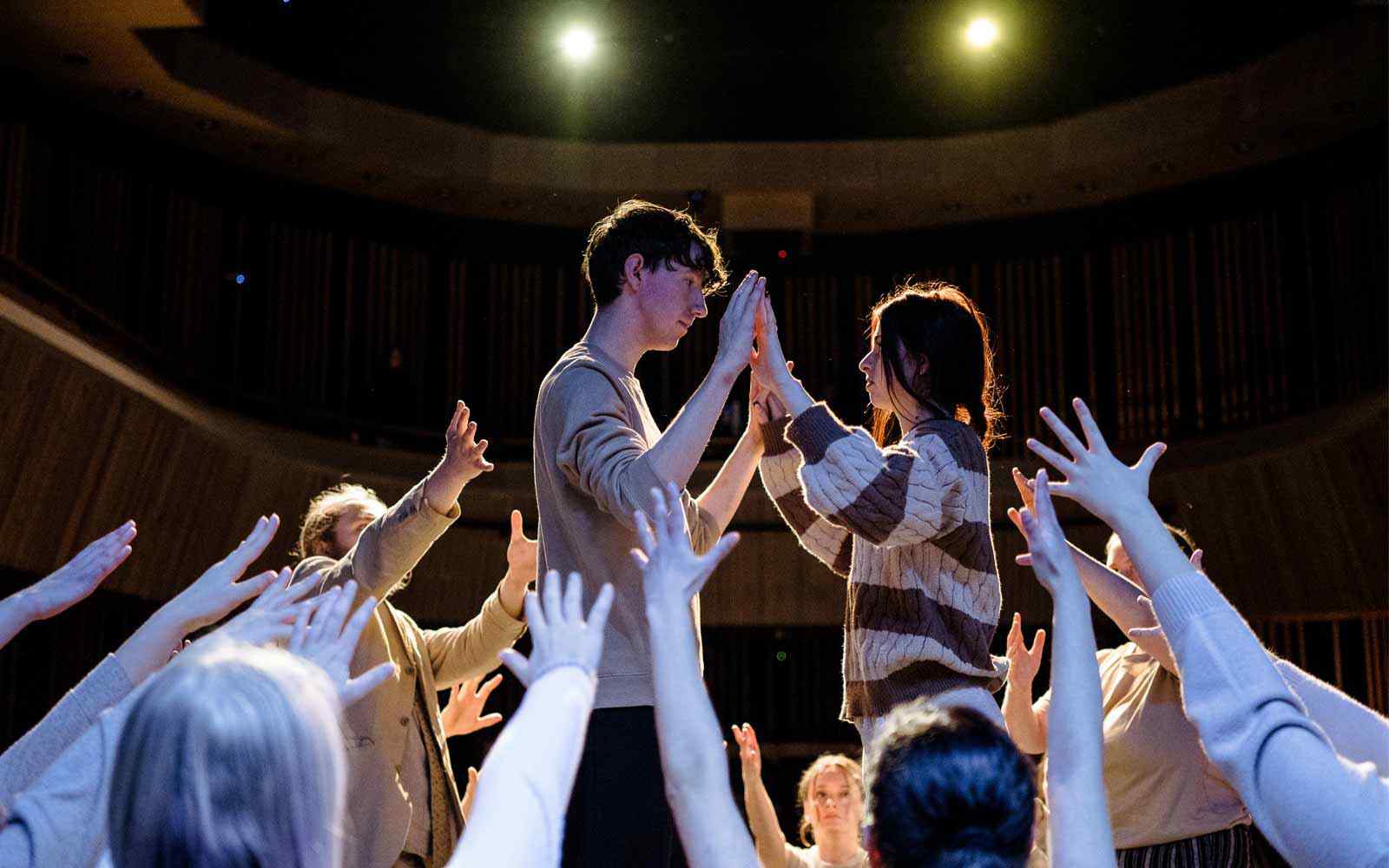 Two theatre students performing surrounded by group.