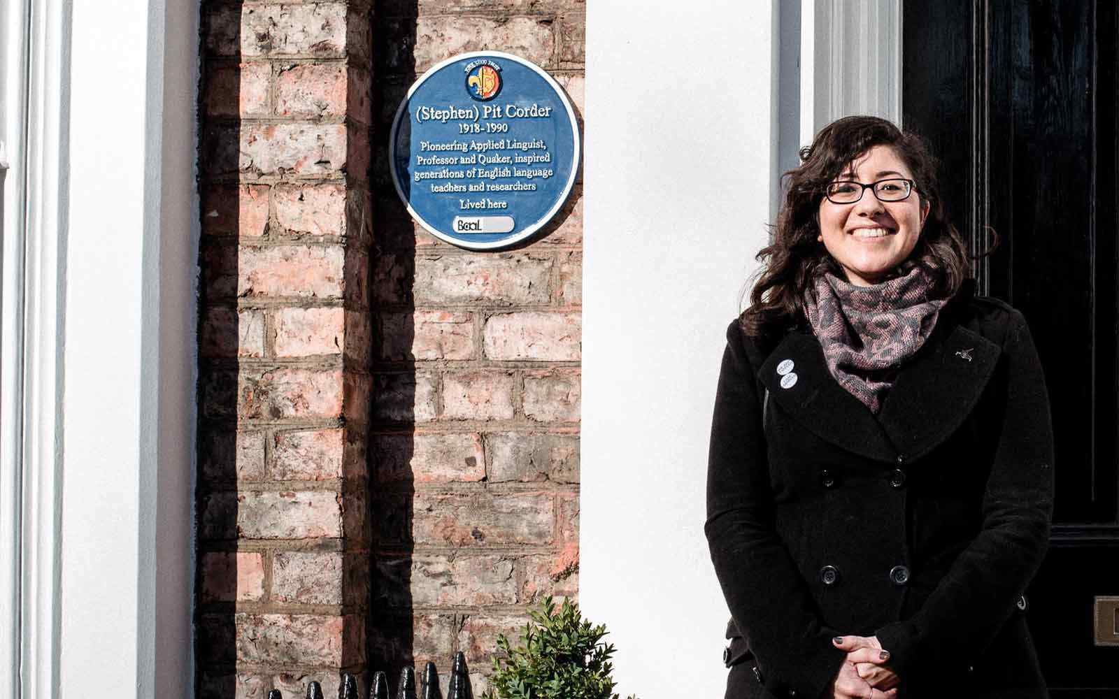 Woman standing next to historic blue plaque.