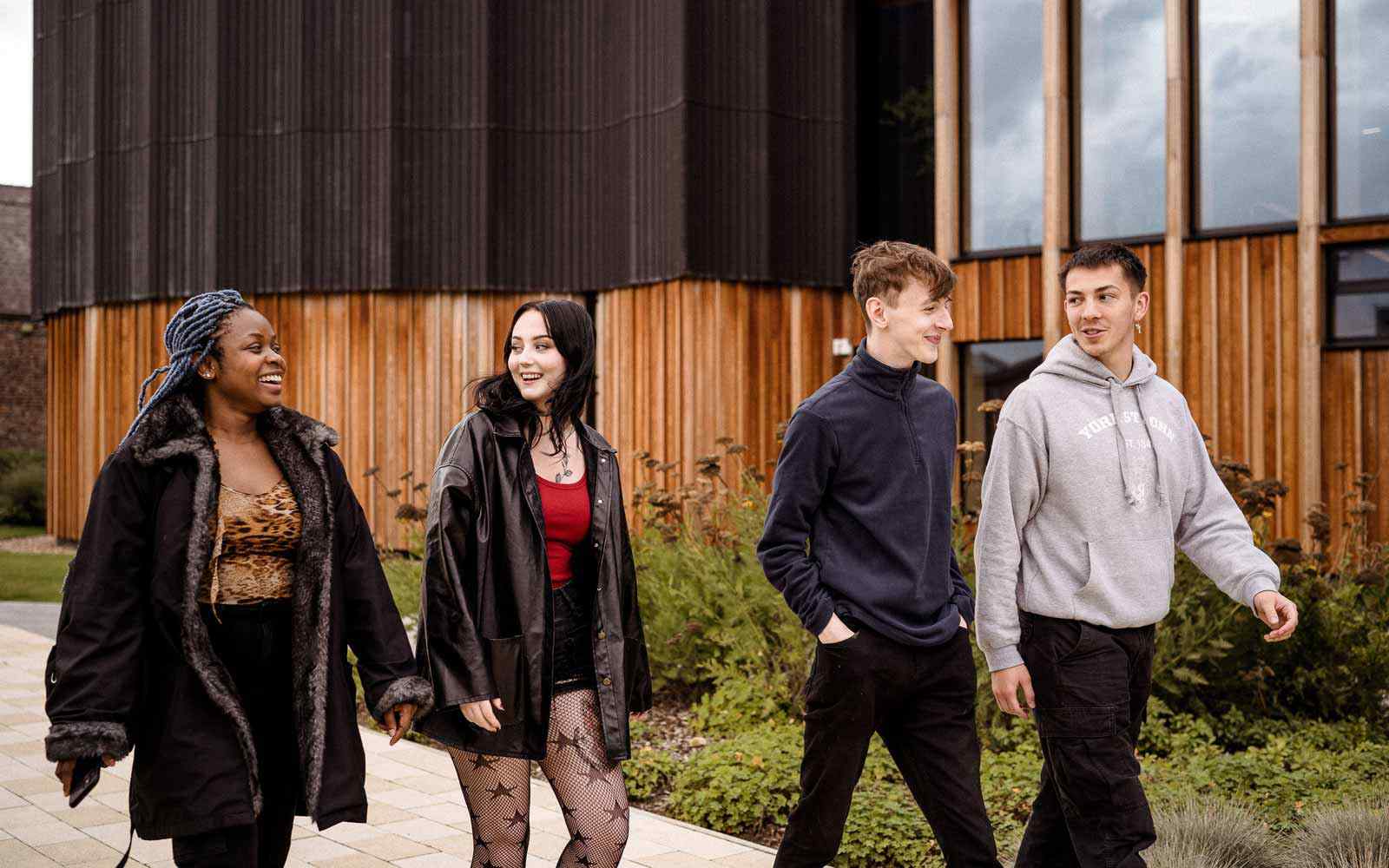 Four students walk and talk together in front of the Creative Centre on campus.