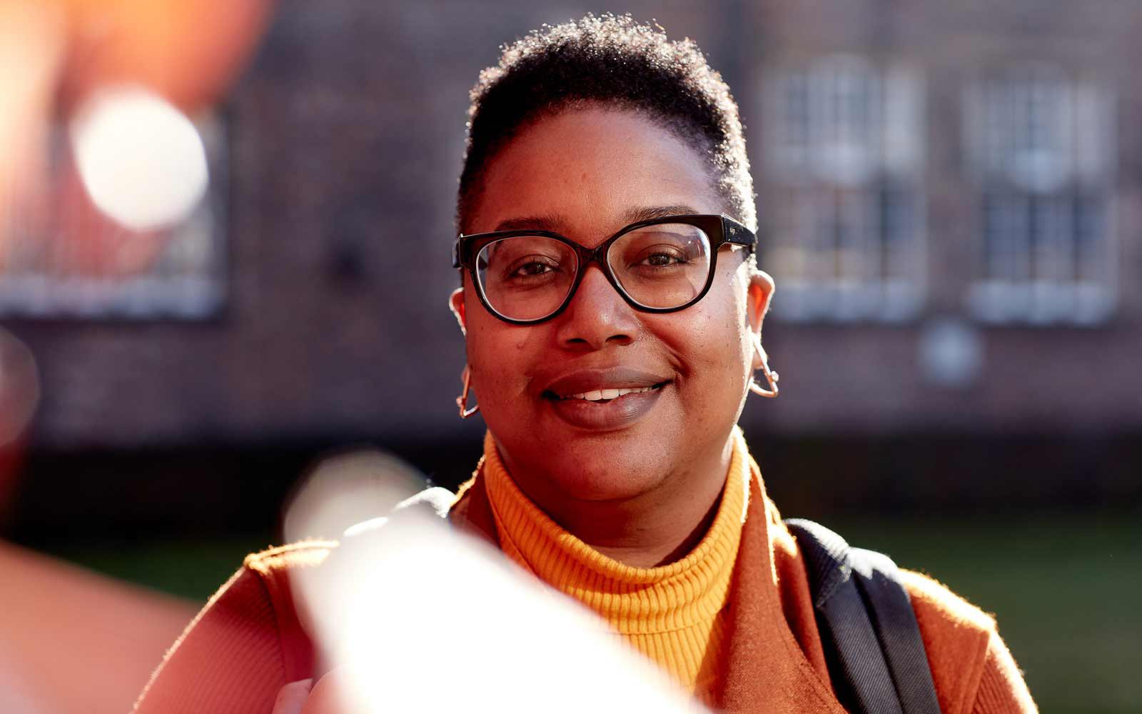 Student with glasses and yellow jumper standing outside