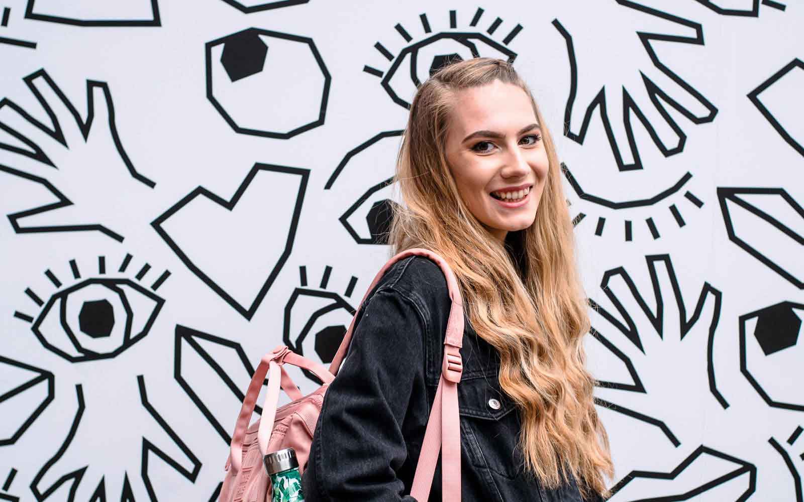 Student wearing bag in front of graffiti wall