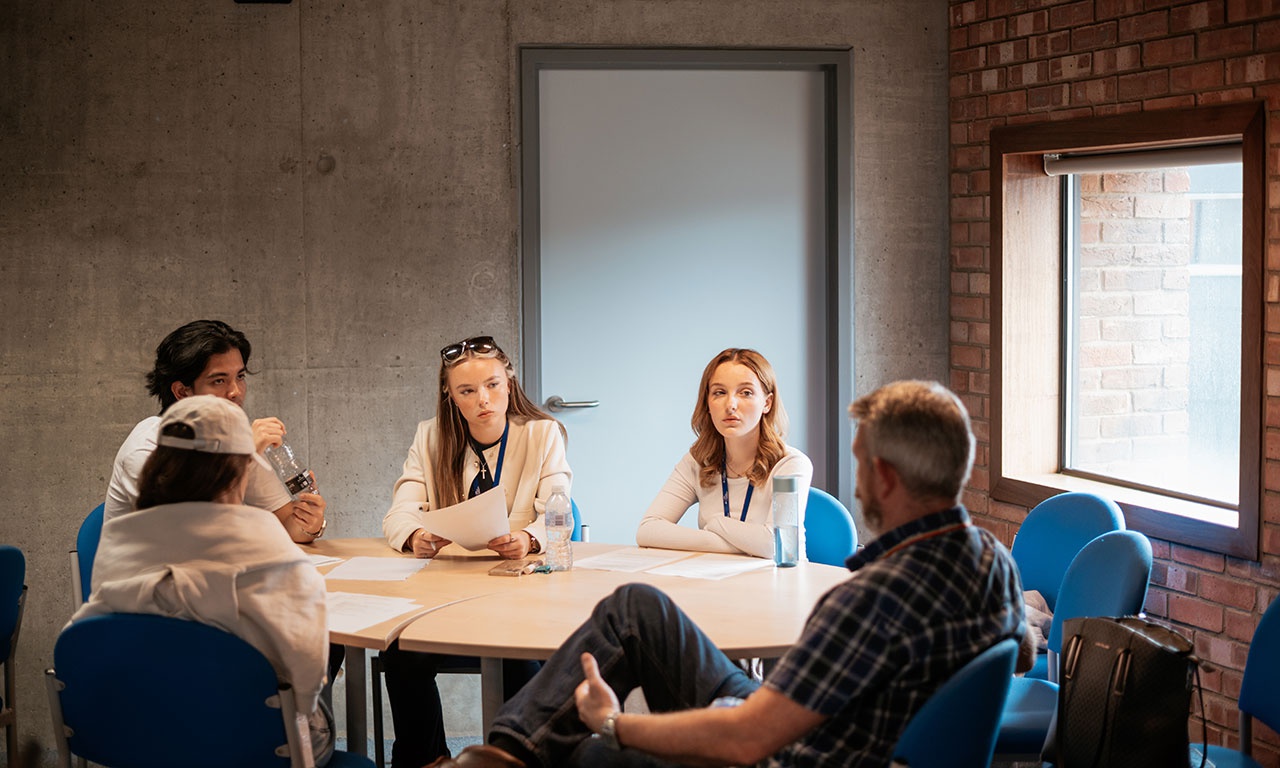 Small group of students in discussion around table with lecturer 