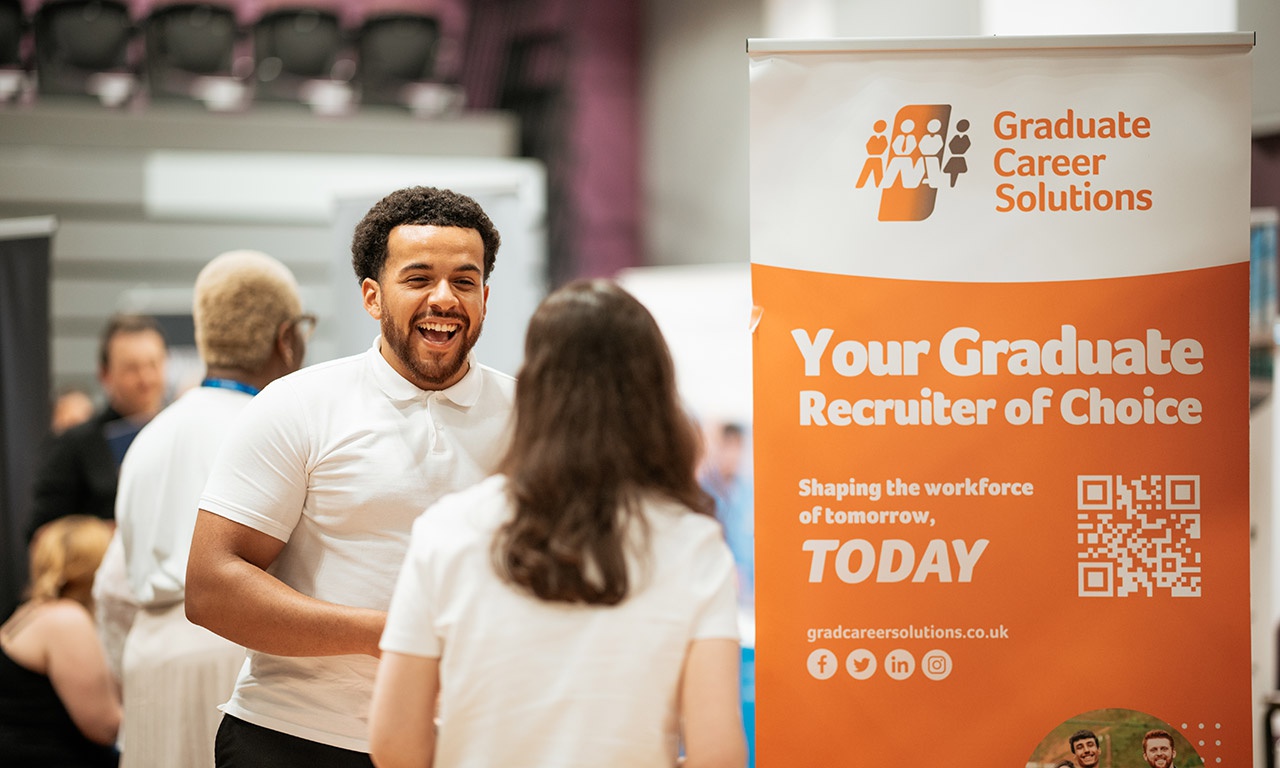 Representative talking to student next to Graduate Career Solutions roller banner 