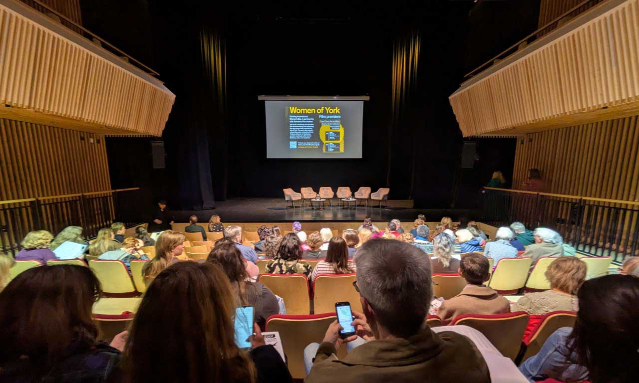 View of back of audience, looking towards stage at Women of York film premiere. 