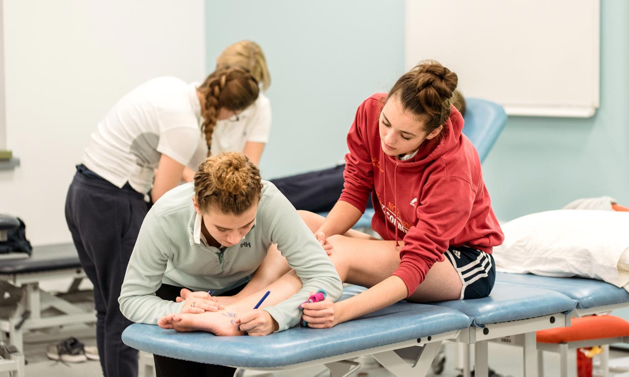 Student writing on ankle of person on physiotherapy treatment bed 