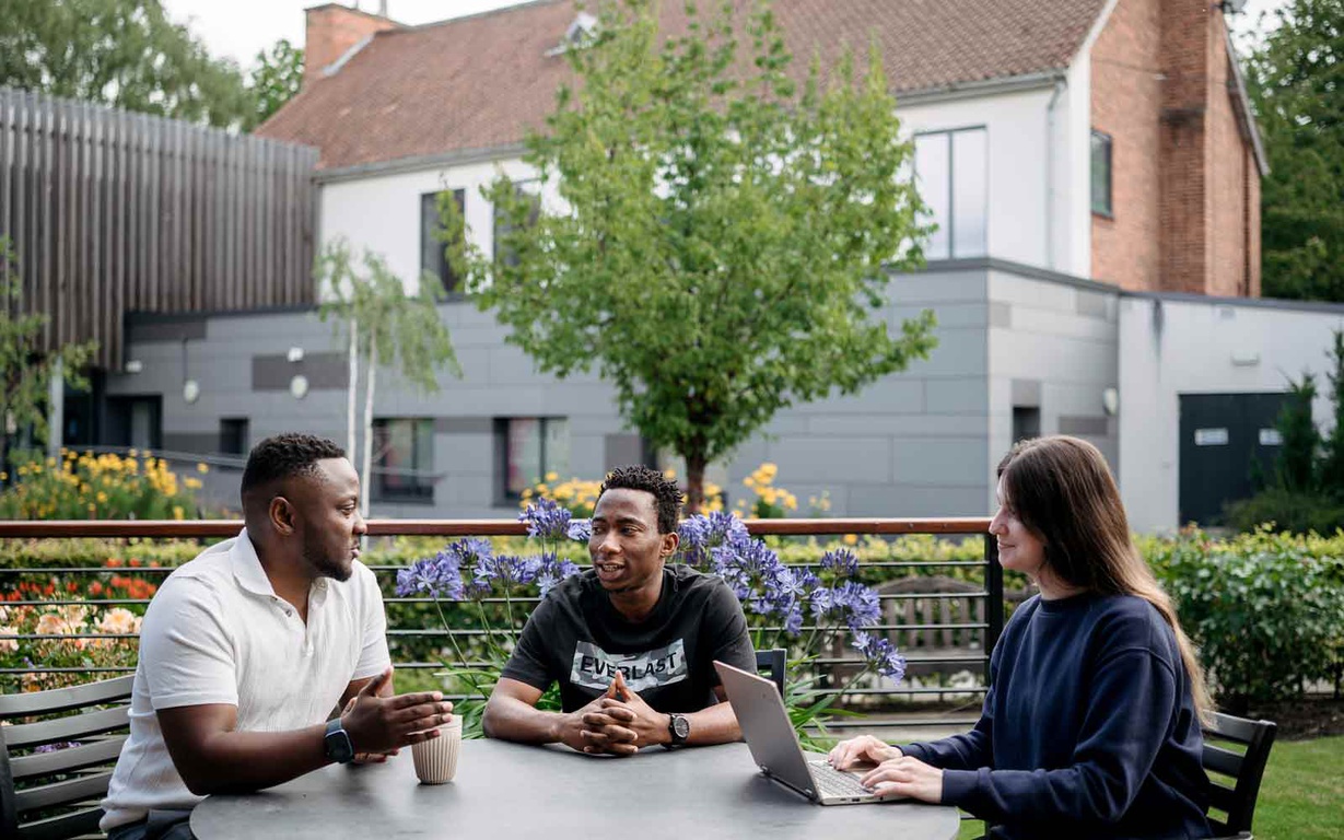 Students sitting at a table outside on York St John University Park campus. 
