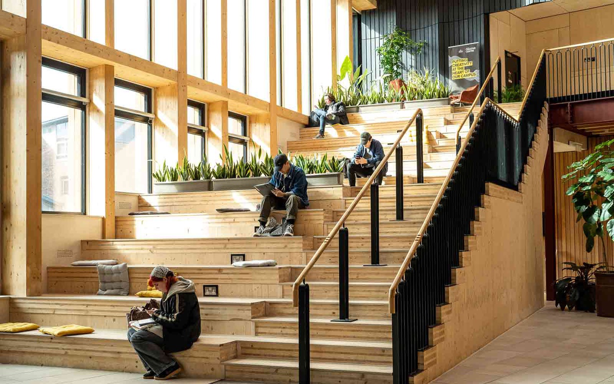 Students seated next to a staircase in the York St John University Creative Centre. 