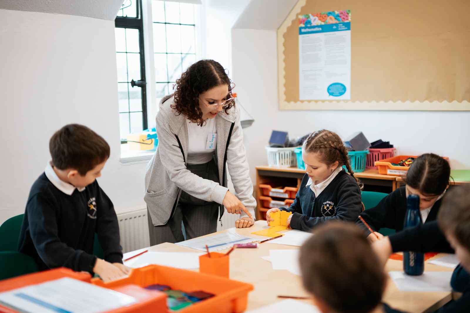 Female trainee teacher attending a table of children in class 