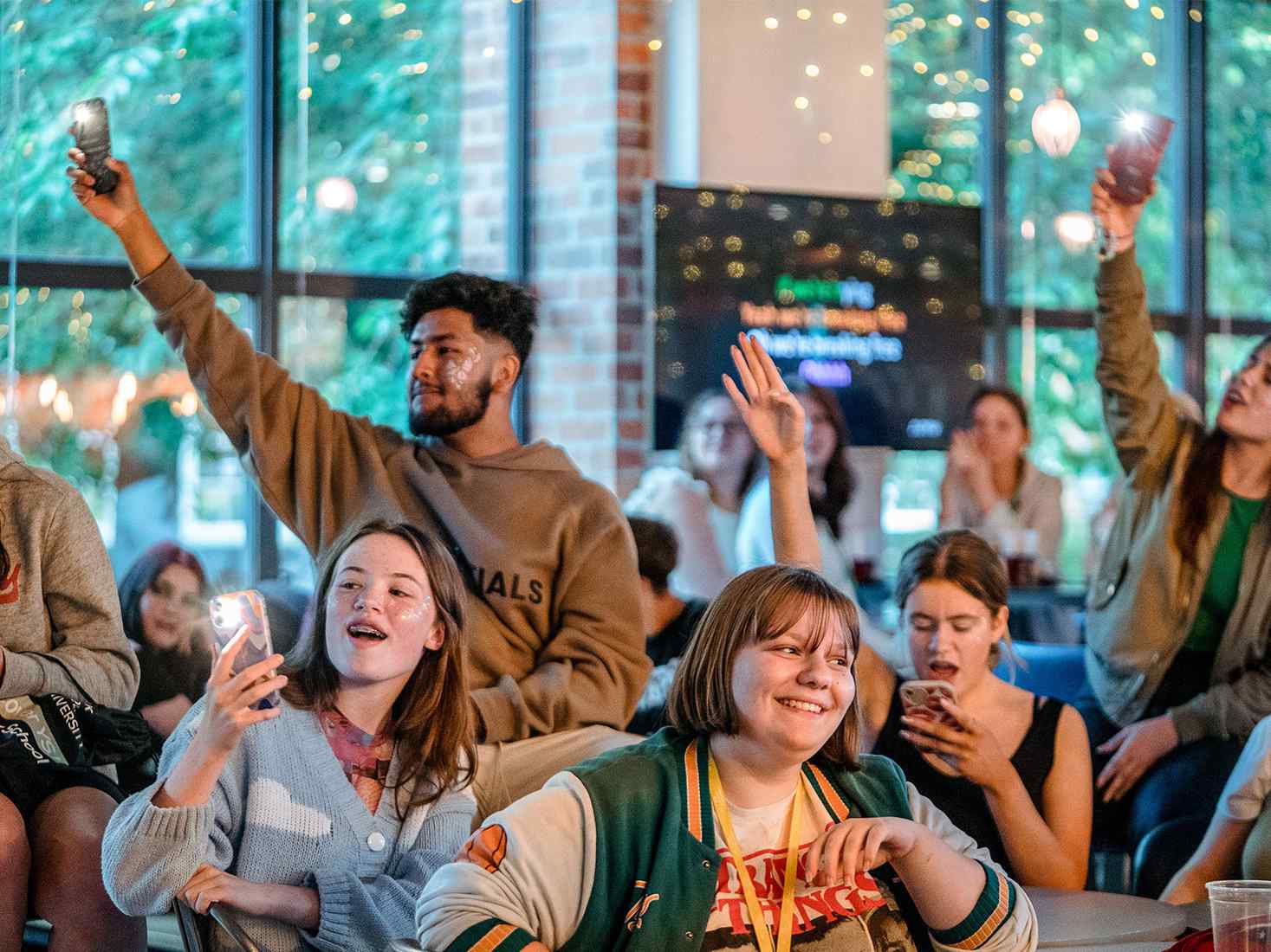 A group of year 12 students singing along to music with their phones with torches on in the air 