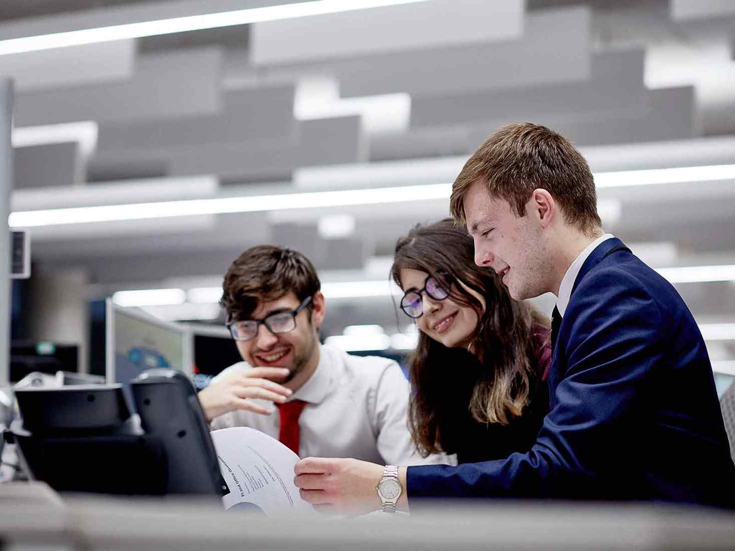 Three students work together at a laptop. 