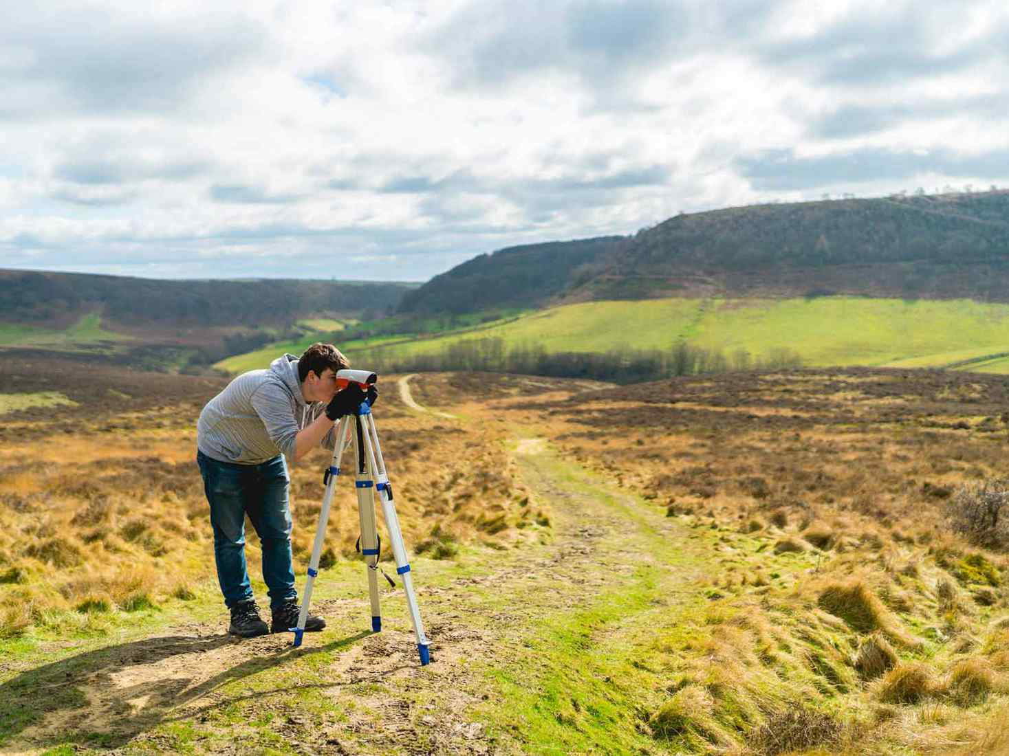 Student looking through surveying tool on Geography field trip. 