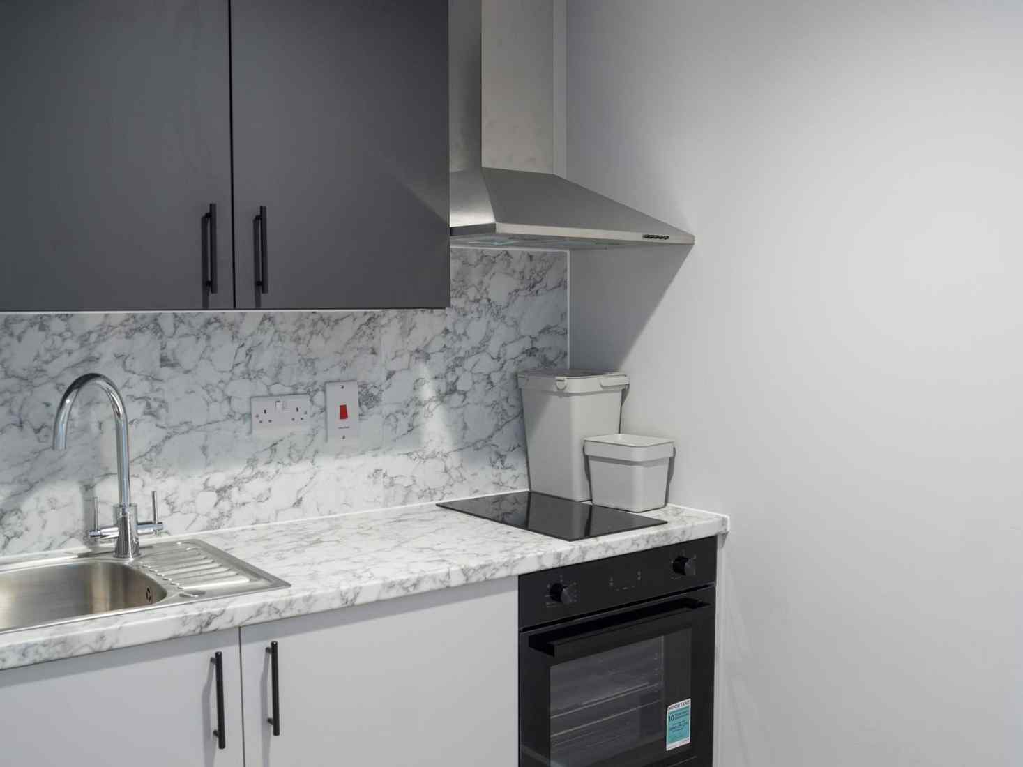 An image of a studio Kitchen in 79 Clarence Street accommodation, including a table, stove, window, and cupboards 
