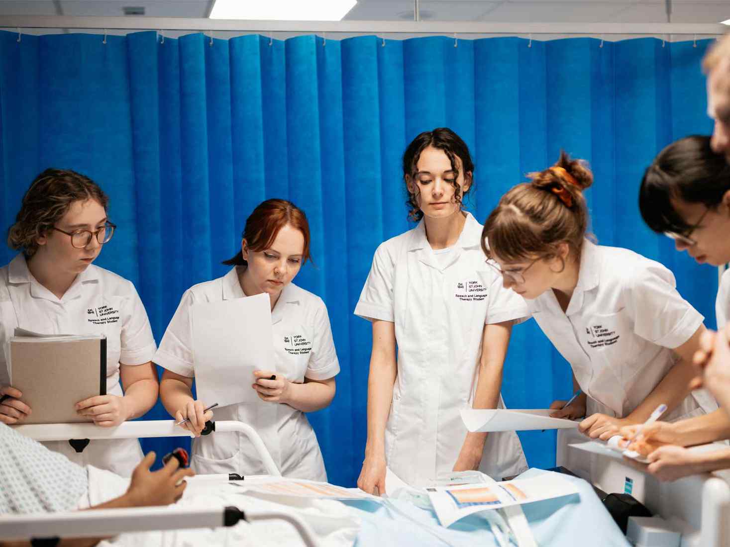 Several students working around a hospital bed in a mock ward setting. 