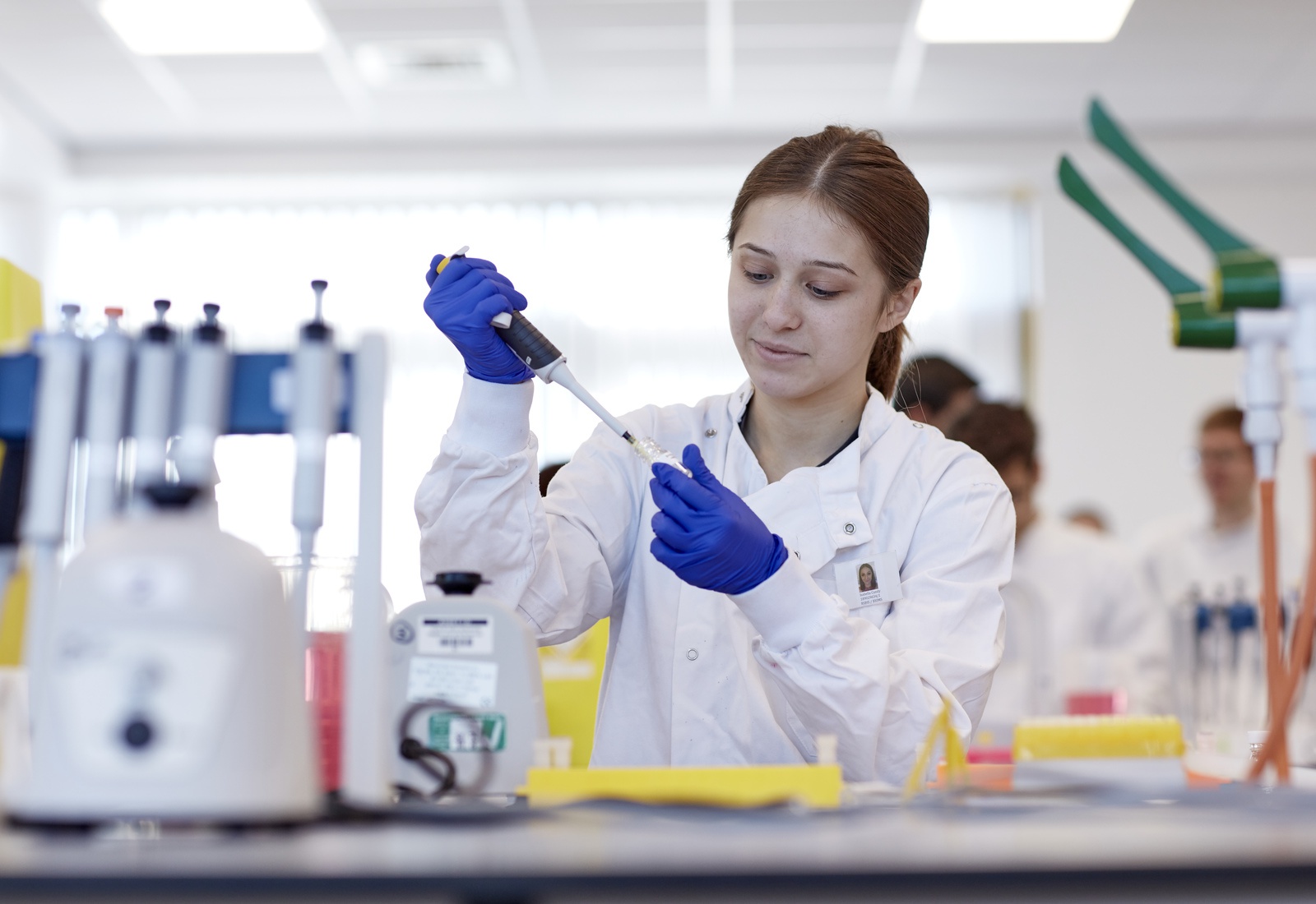A student in a lab coat holding a pipette and test tube 