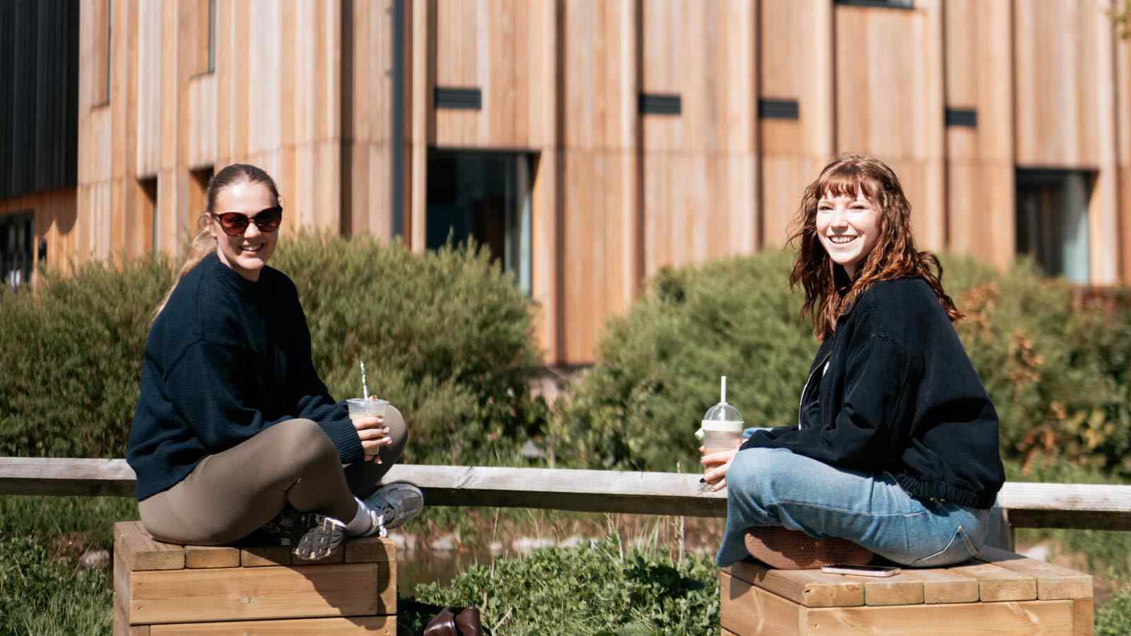 Two students with iced drinks, sitting outside on campus. 